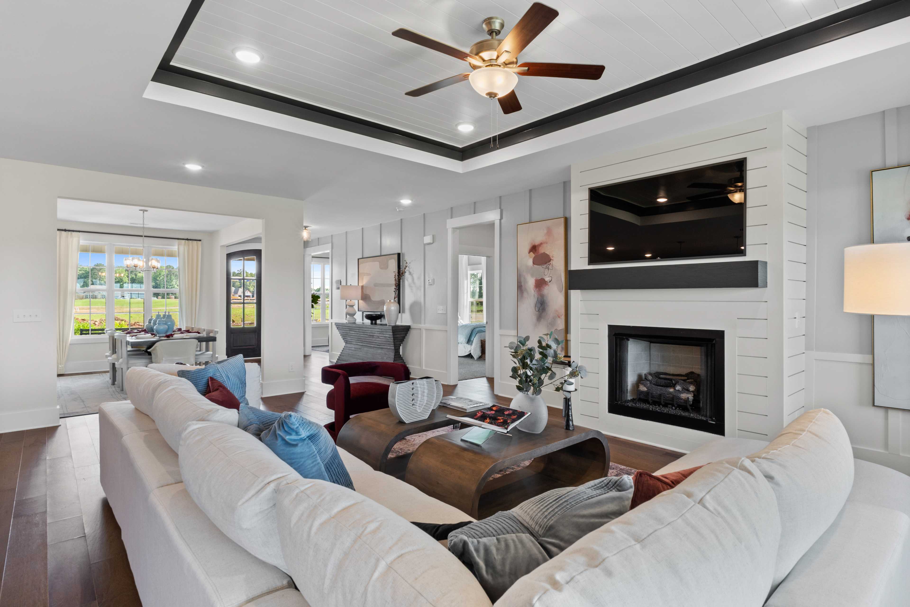 Open-concept living room in Creekside Harvest Alabama with white shiplap walls, gas fireplace, mounted TV, ceiling fan, and plush sectional sofa