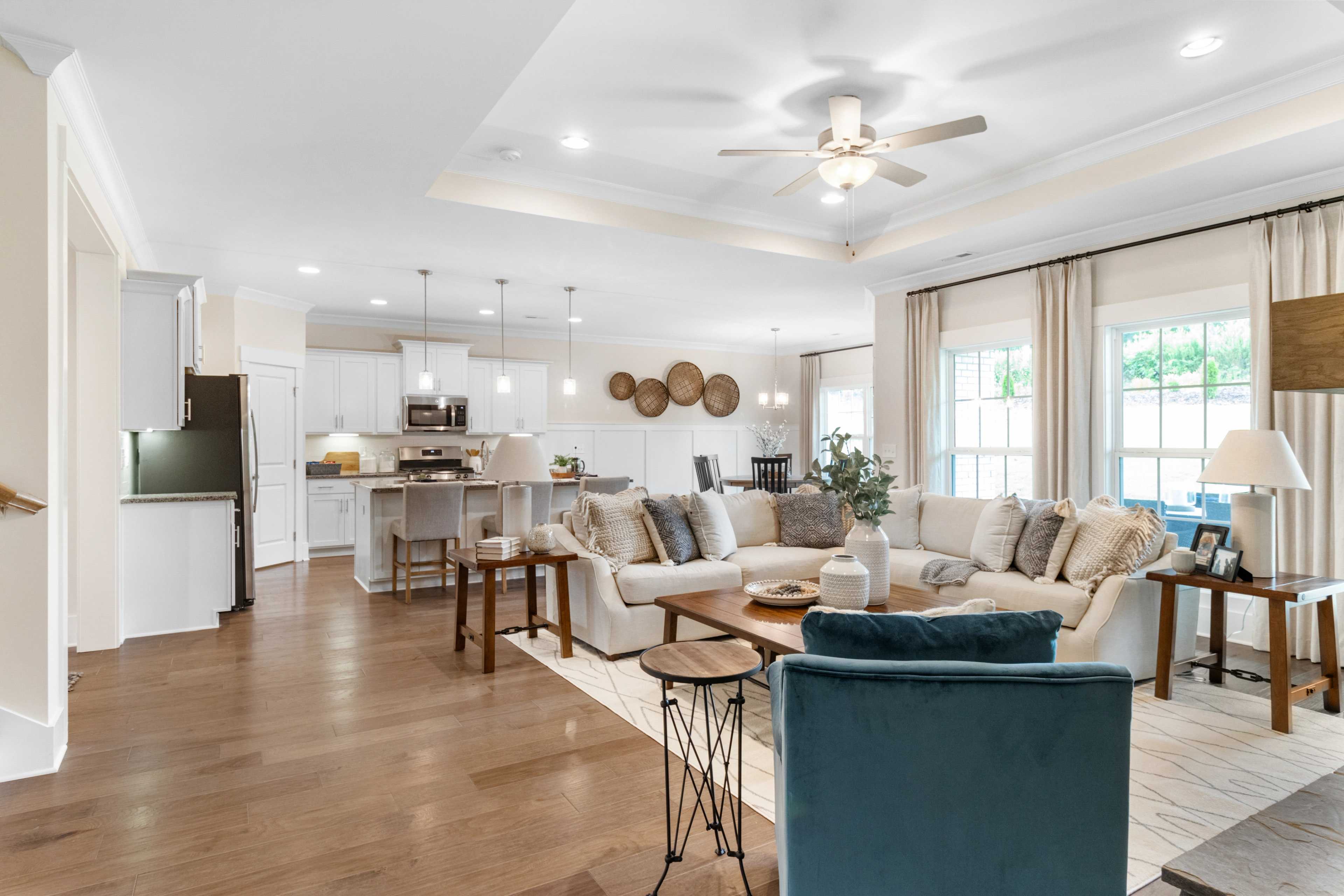 Open-concept living room and kitchen at Noble Ridge in Cullman Alabama with hardwood floors, beige sofas, and white island