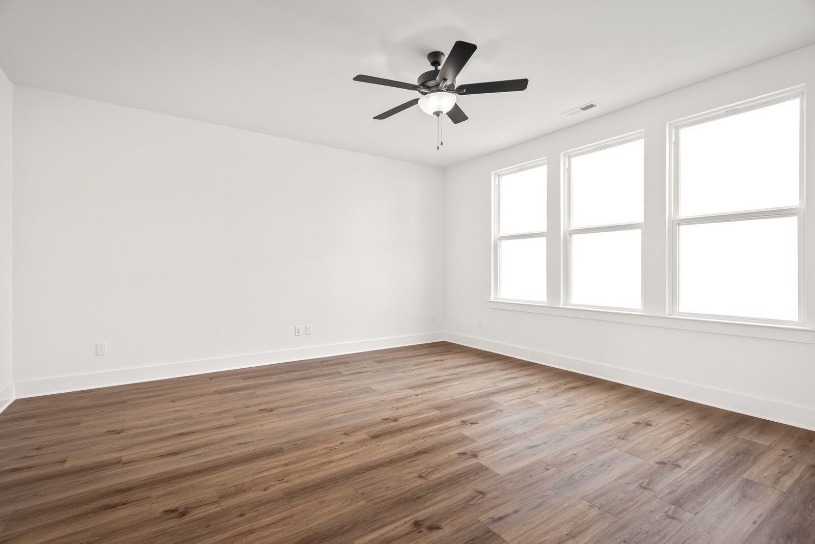 Bright bedroom with hardwood floors, white walls, ceiling fan, and triple windows in Davidson Homes The Logan C, Gallatin, TN