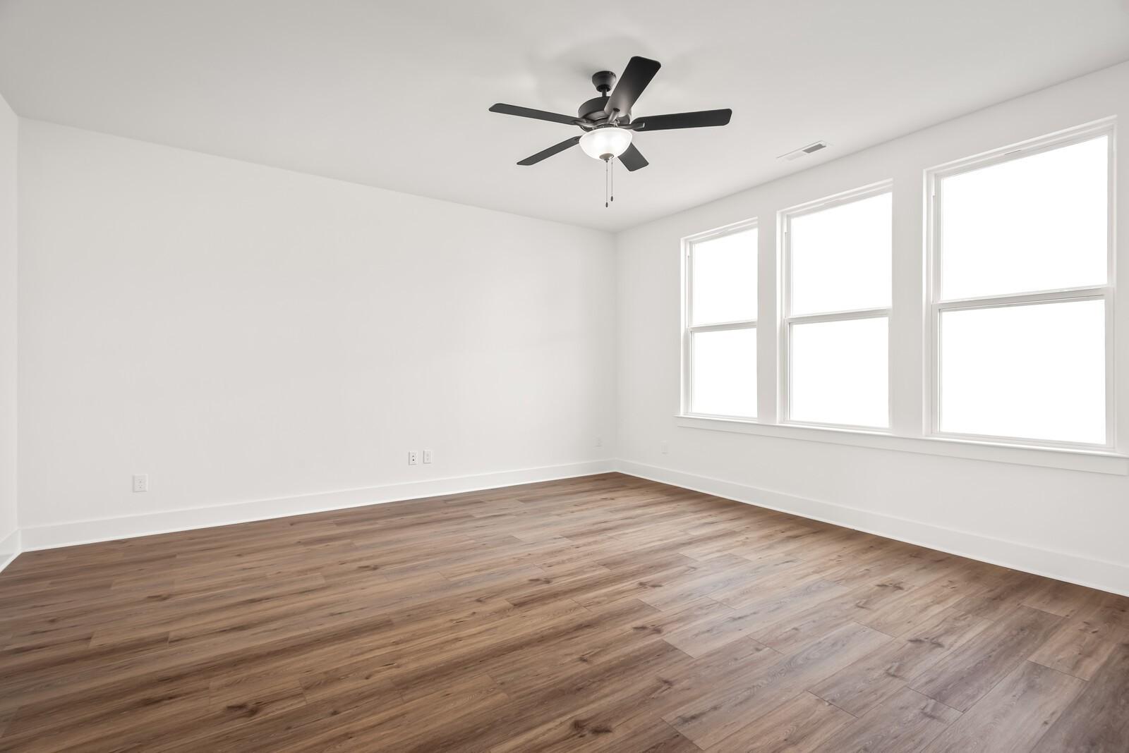 Bright bedroom with hardwood floors, white walls, ceiling fan, and triple windows in Davidson Homes The Logan C, Gallatin, TN