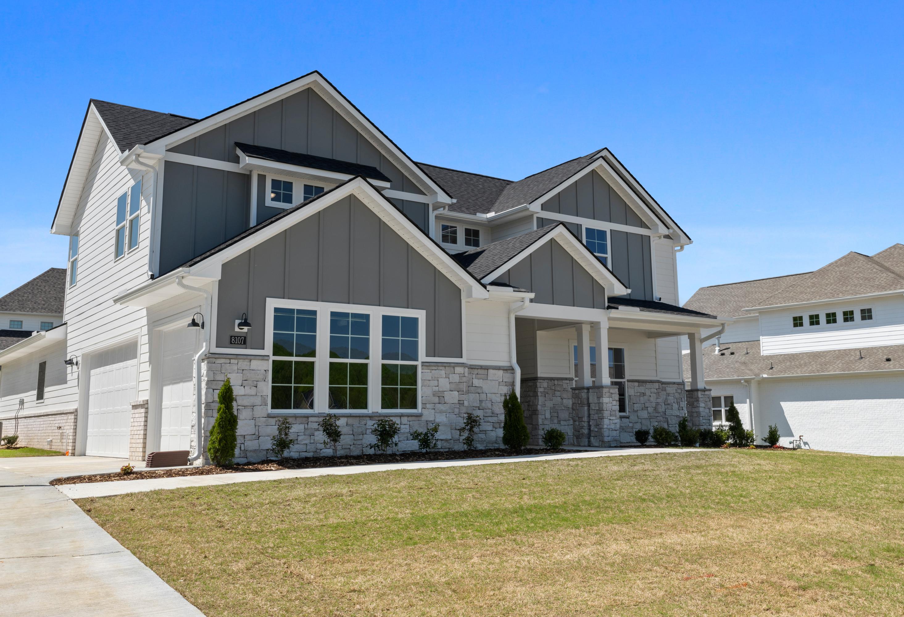 Modern single-story facade of The Haven D with gray shake siding, stone pillars, 3-car garage, and covered porch in Owens Cross Roads