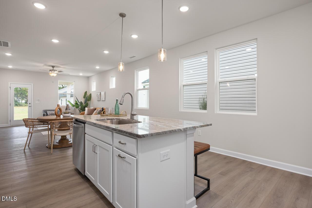 Open-concept kitchen with granite island sink, white cabinets, bar stools, and dining nook in The Carter C 3-bedroom home, Lillington, NC