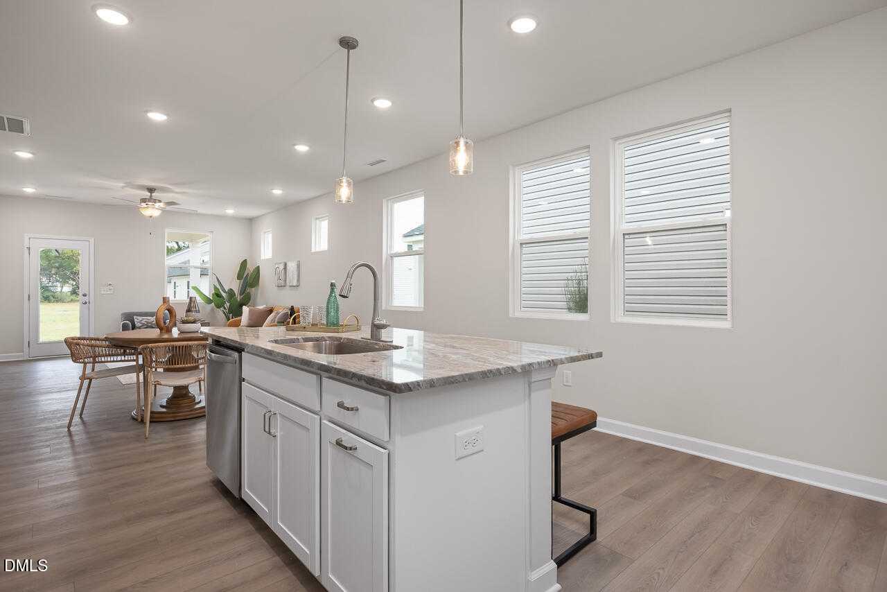 Modern open-concept kitchen with white cabinets, granite island sink, pendant lights, and bar stools in The Carter C by Davidson Homes, Lillington NC