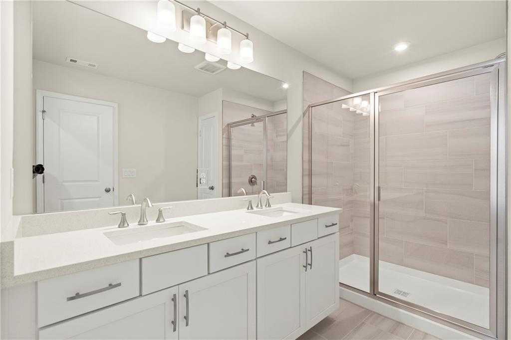 Elegant master bathroom with double vanity, white cabinets, frameless glass shower, and beige tile in Davidson Homes The Cary A, Kennesaw, Georgia