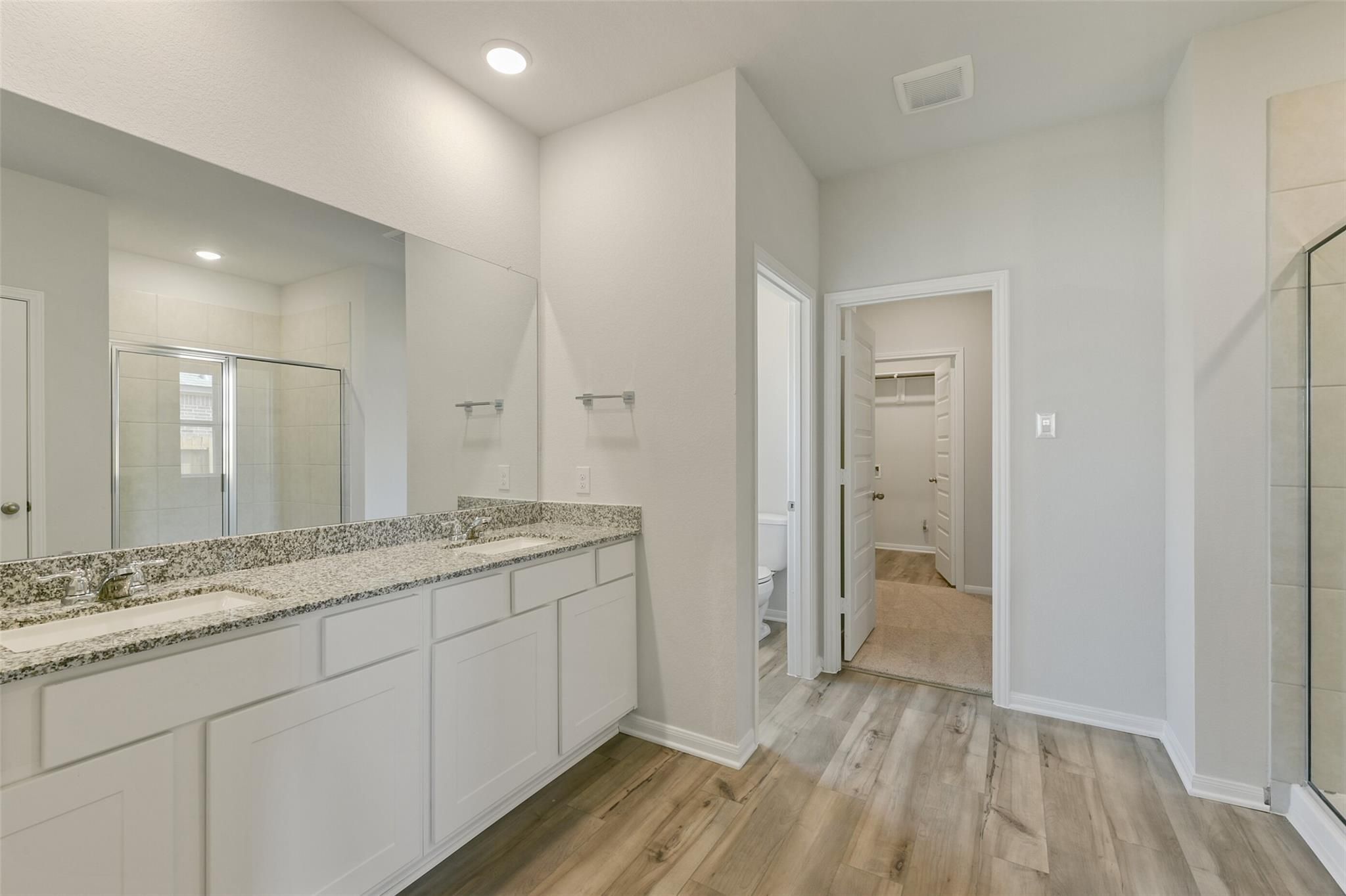 Modern master bathroom featuring double granite vanity, frameless shower, and hardwood floors in Davidson Homes The Laguna B, Dayton, Texas