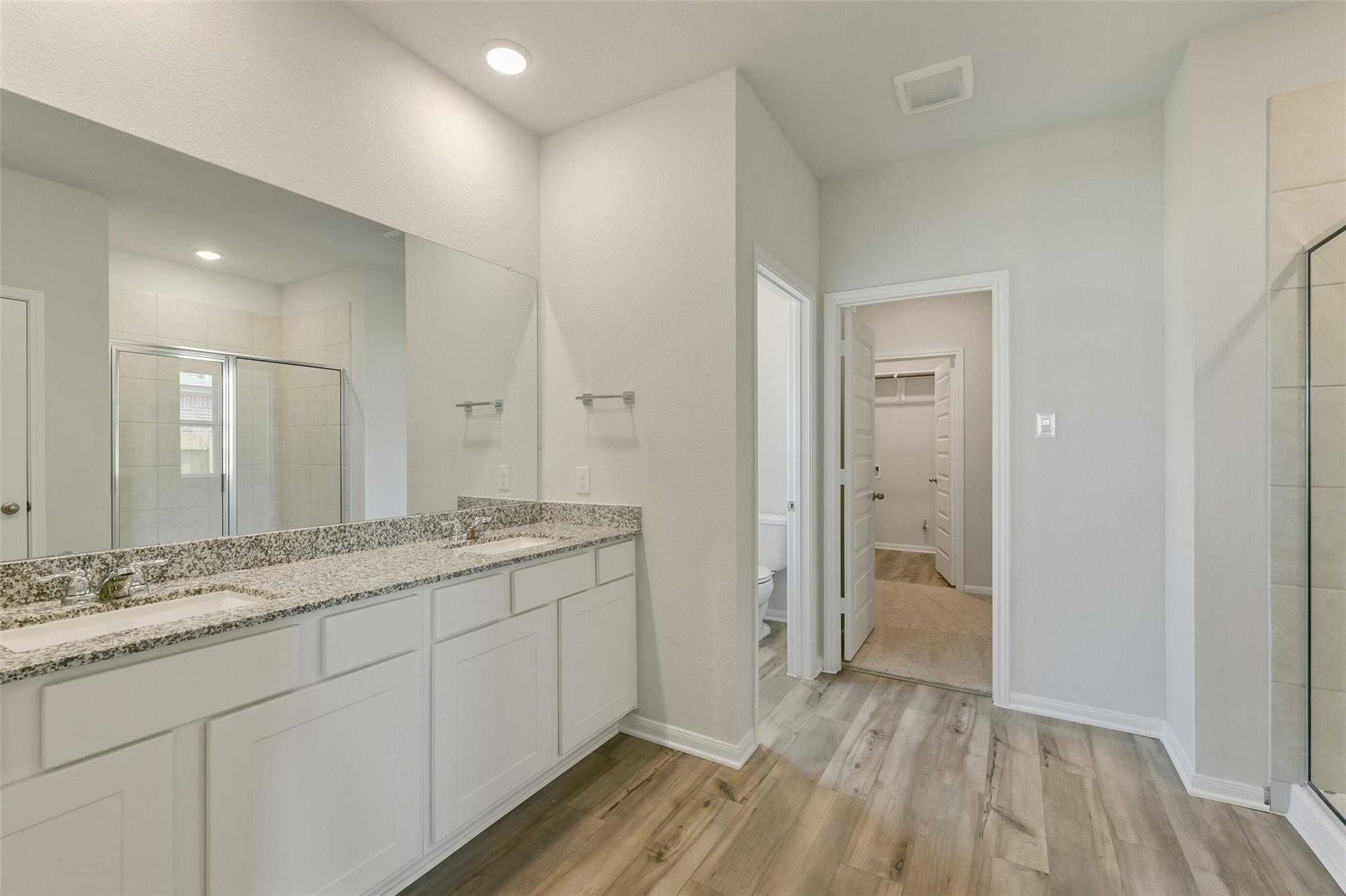 Modern master bathroom featuring double granite vanity, frameless shower, and hardwood floors in Davidson Homes The Laguna B, Dayton, Texas