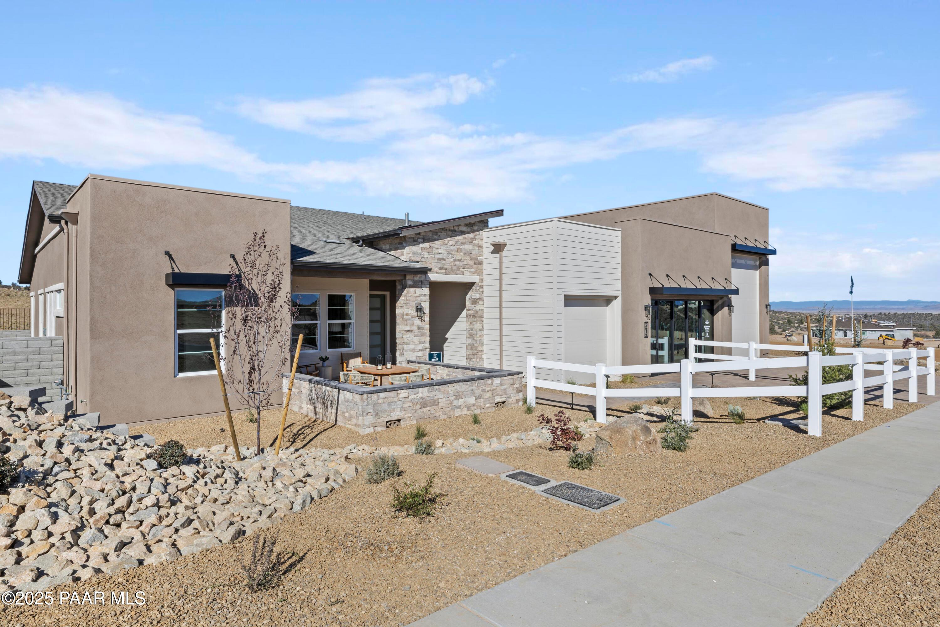 Modern 1-story stucco home exterior with covered entry, desert rock landscaping, white fence in Hidden Hills, Prescott, Arizona