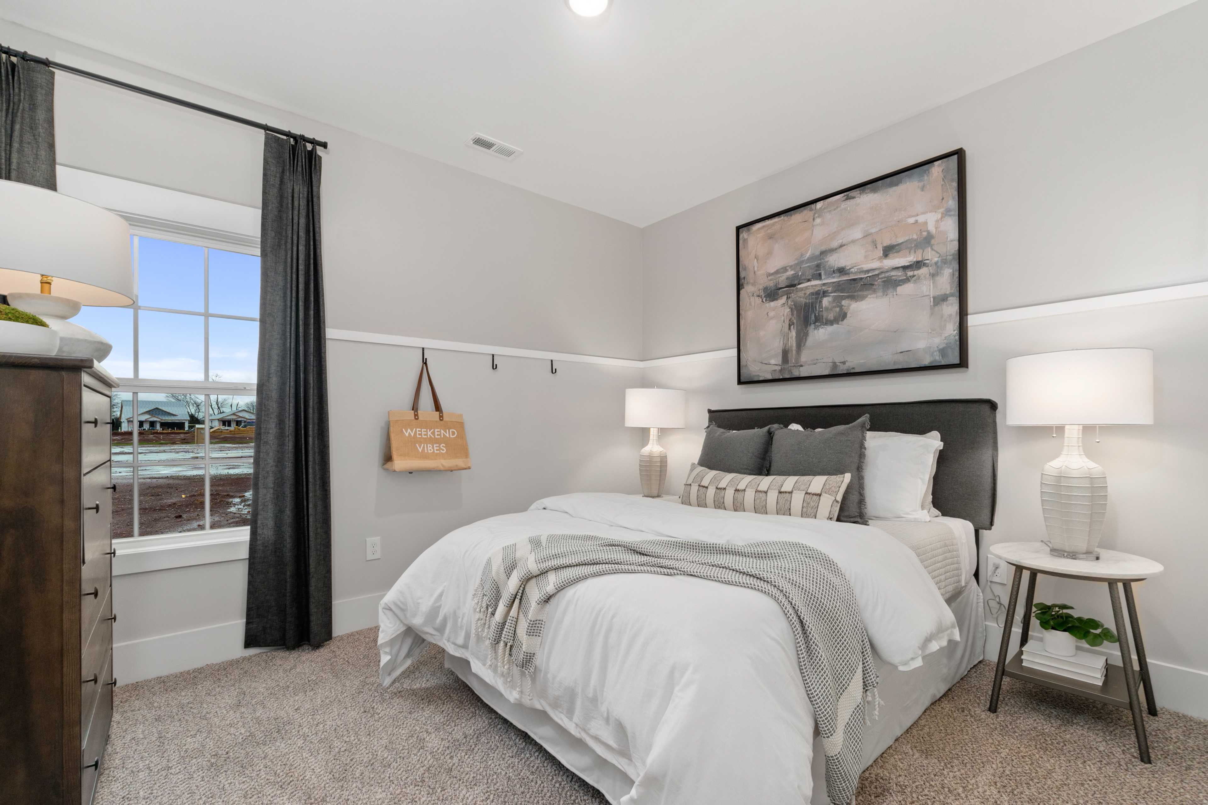 Spacious bedroom at Kendall Farms in Toney AL featuring gray walls, king bed with white duvet, abstract wall art, and bedside lamps