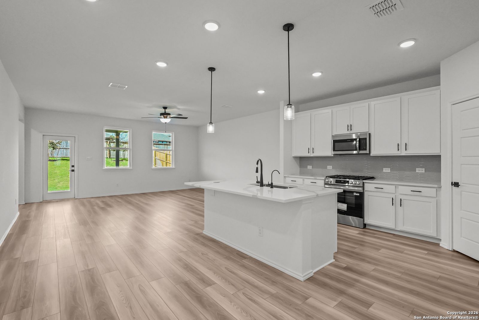 Bright open kitchen with white island, stainless appliances, pendant lights in Davidson Homes The Douglas E, Comanche Ridge, San Antonio