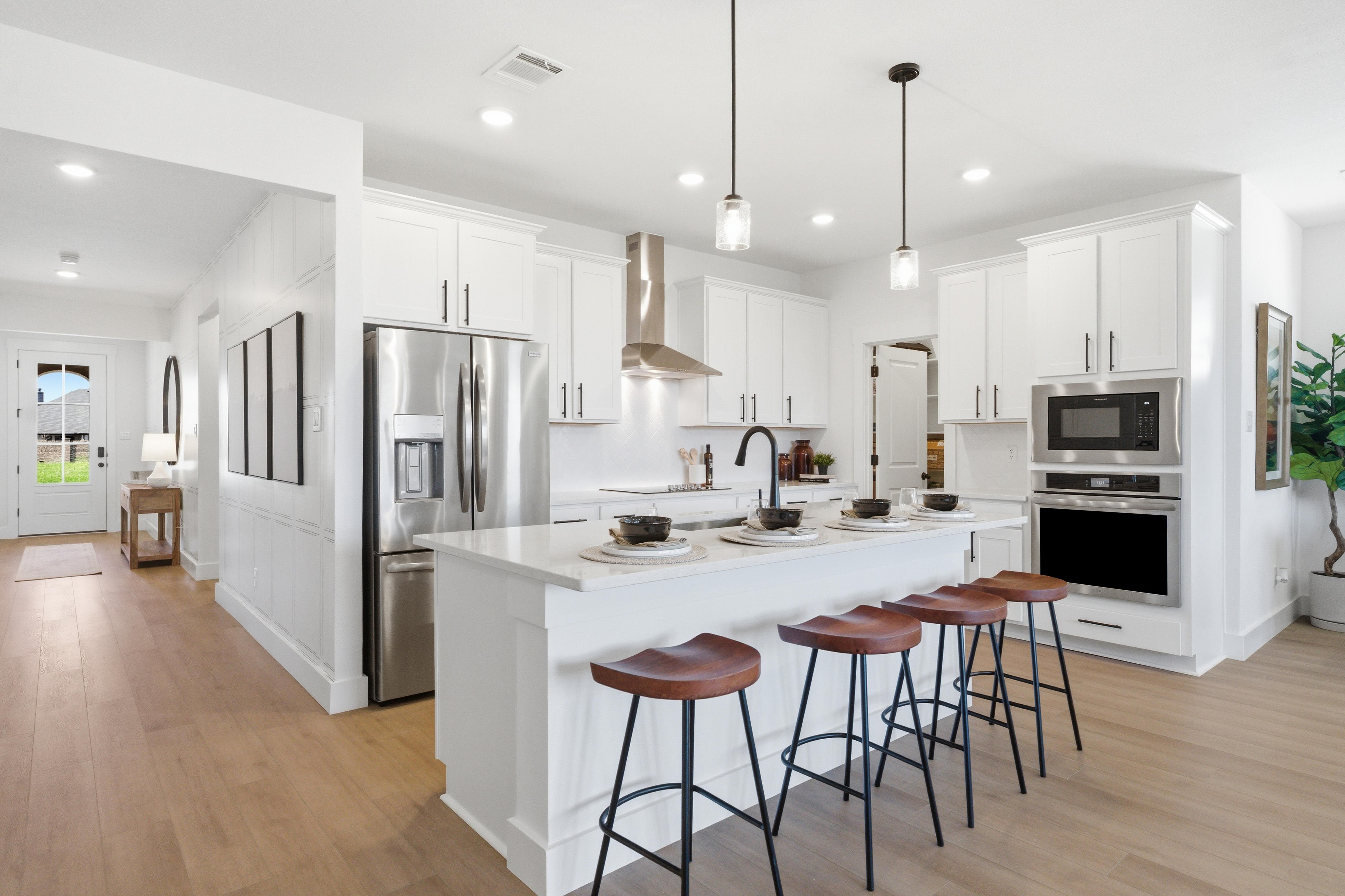 Spacious white kitchen in Mercer Meadows Royse City TX with island bar stools stainless appliances and hardwood floors