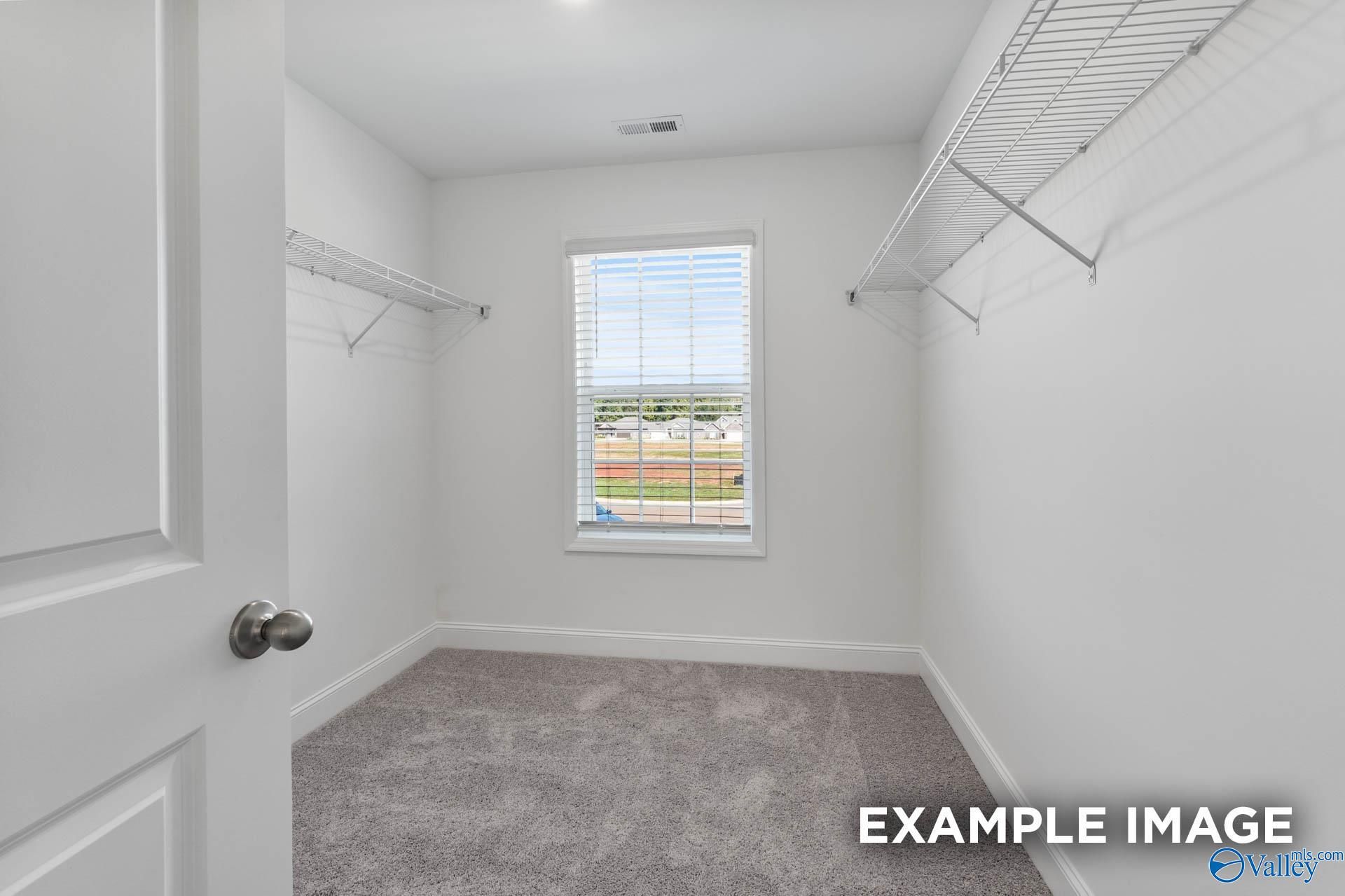 Spacious walk-in closet with wire shelving, hanging rods, and window view in Davidson Homes The Shelby A, Hazel Green, Alabama