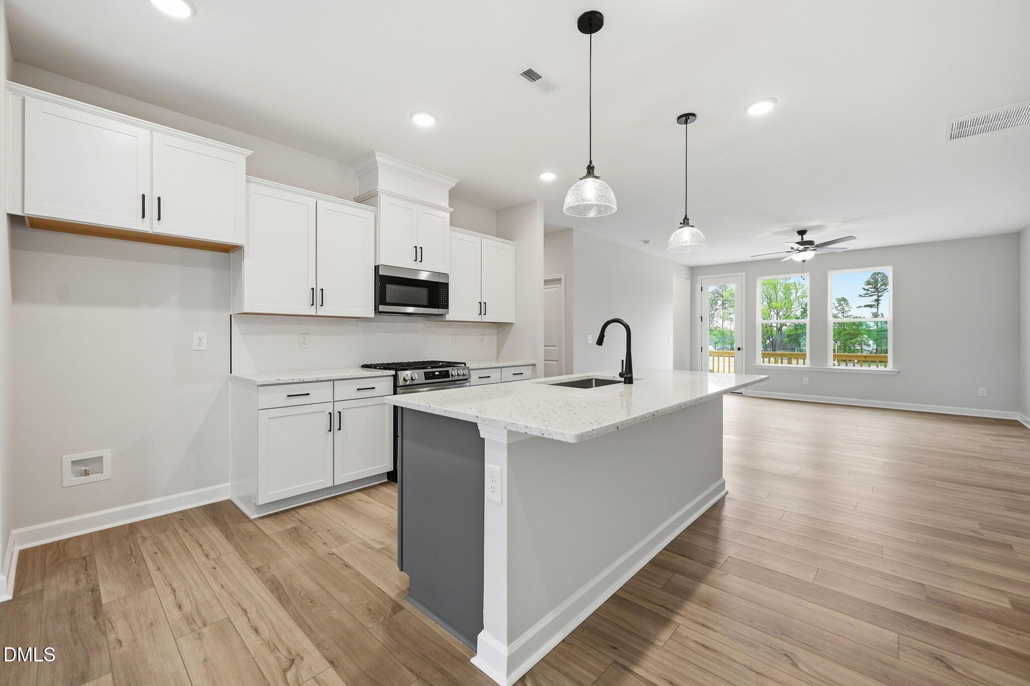 Modern kitchen with white cabinets, center island, and wood-style flooring in The Mitchell floor plan, Camden Park, NC.