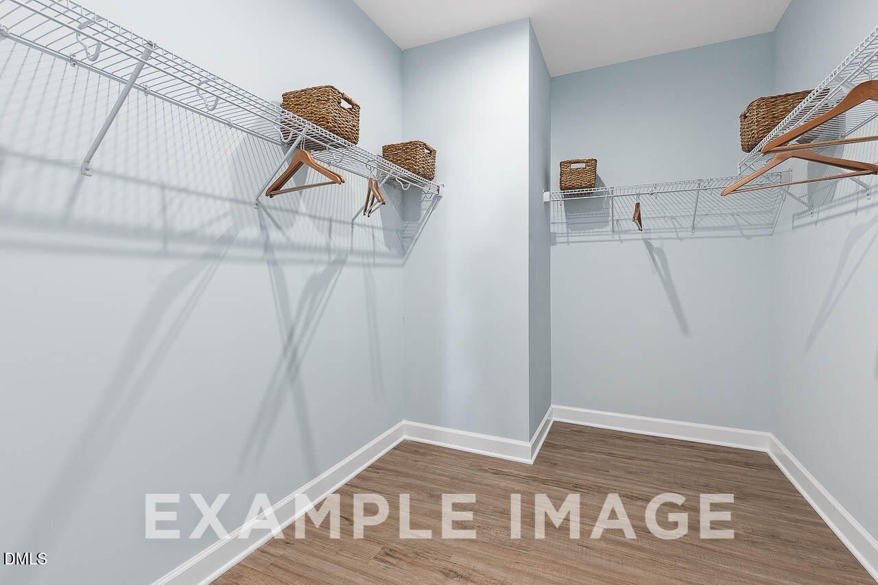 Walk-in closet with wire shelving, wicker baskets, and wood-look flooring in Davidson Homes The Ash C, Lillington, North Carolina