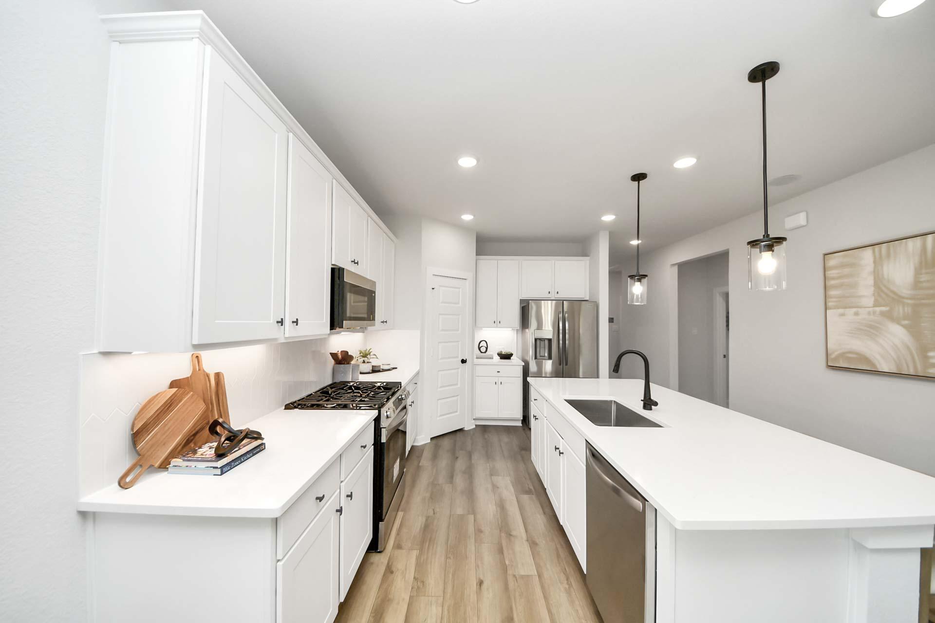 Modern kitchen at Enclave at Newport in Crosby, TX with white cabinets, quartz countertops, and stainless steel appliances.