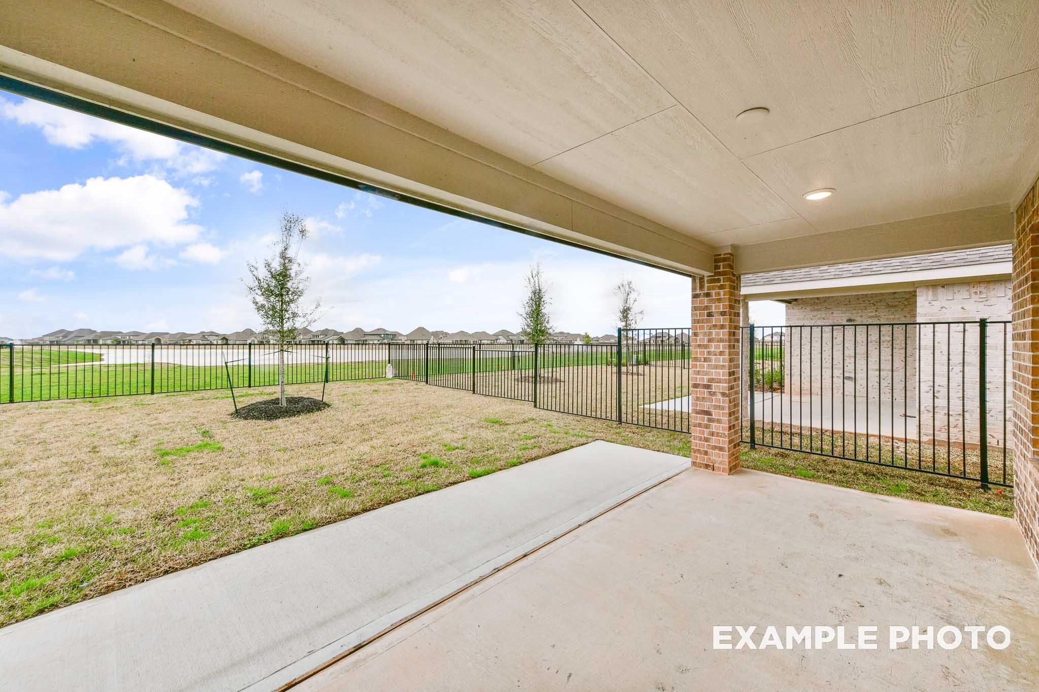 Covered patio of The Laguna A showcasing open backyard with pond, young trees, brick fencing, and Texas sky in Rosharon