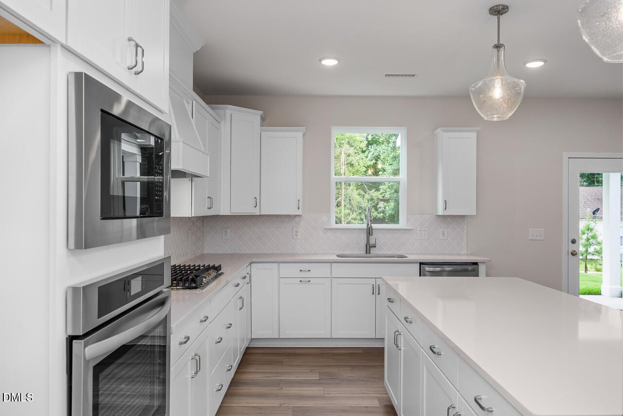 Modern kitchen with white cabinets, quartz island, and stainless appliances in The Hickory II C home, Montrose, Aberdeen, NC.
