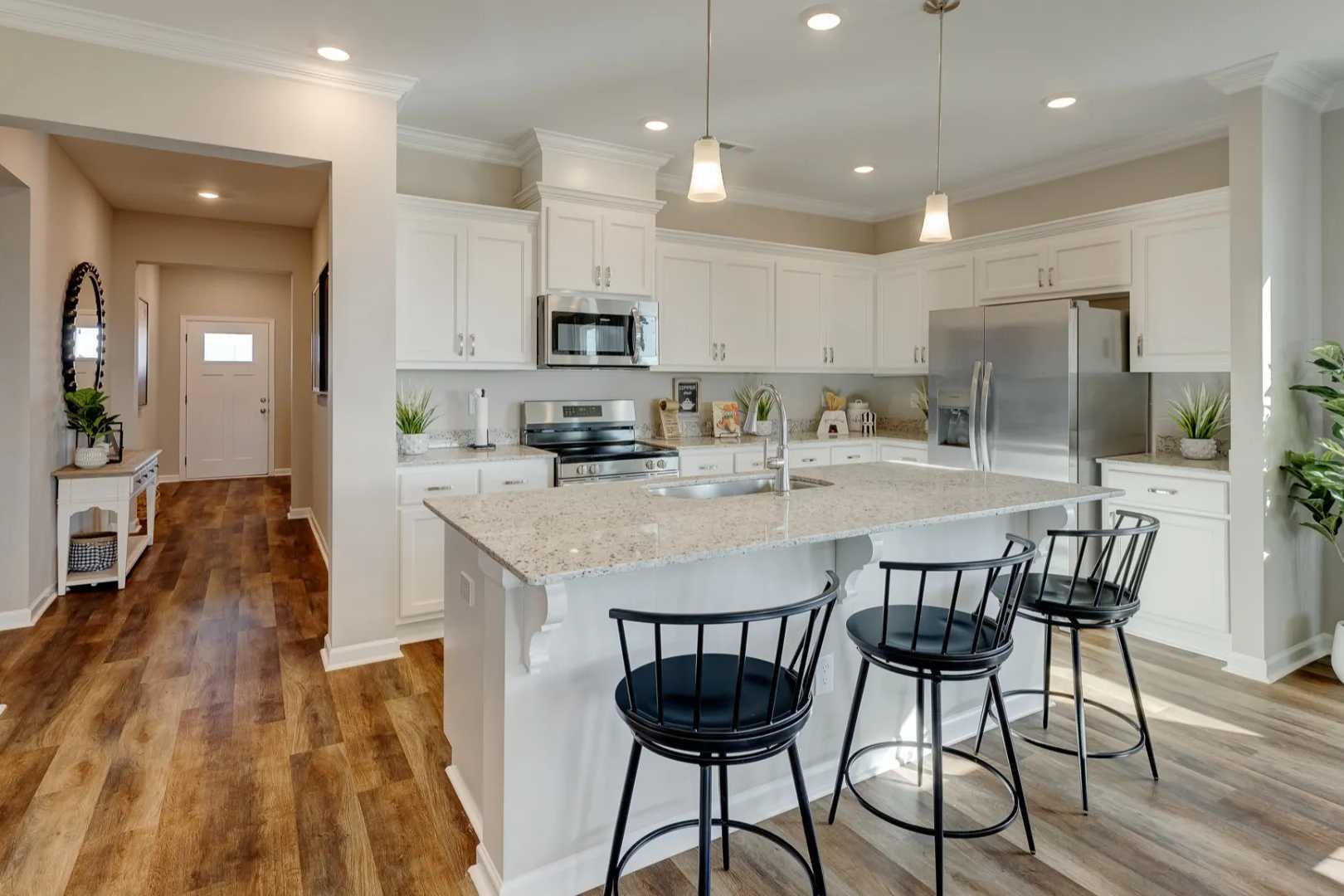 Spacious open-concept kitchen in The Aurora B with white cabinetry, large island, bar stools, stainless appliances, and adjacent entryway