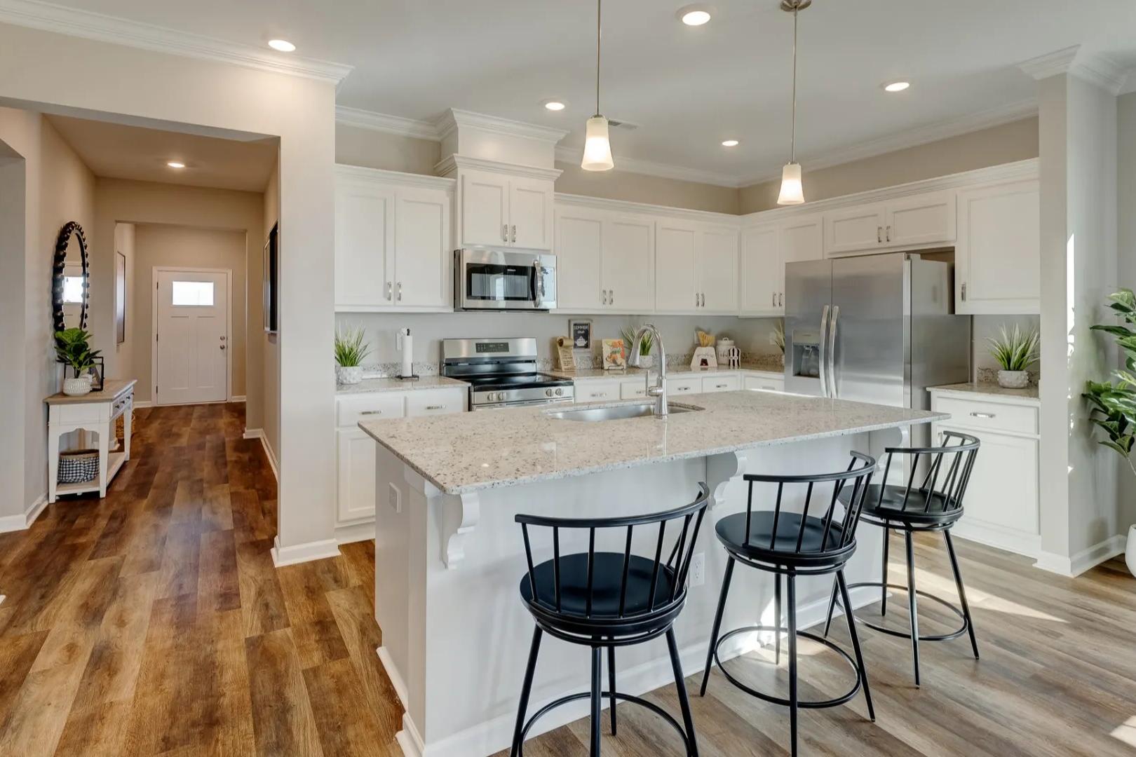 Spacious Aurora A kitchen by Davidson Homes with white shaker cabinets, quartz island, black bar stools, stainless appliances, open to entry