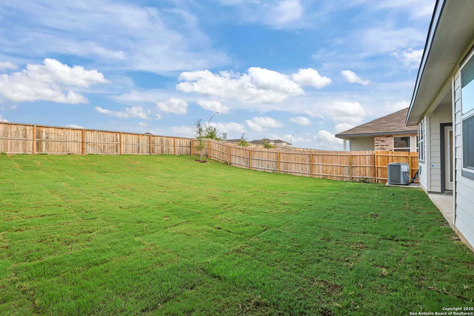 Spacious fenced backyard with lush green lawn beside single-story home in Comanche Ridge, San Antonio, Texas