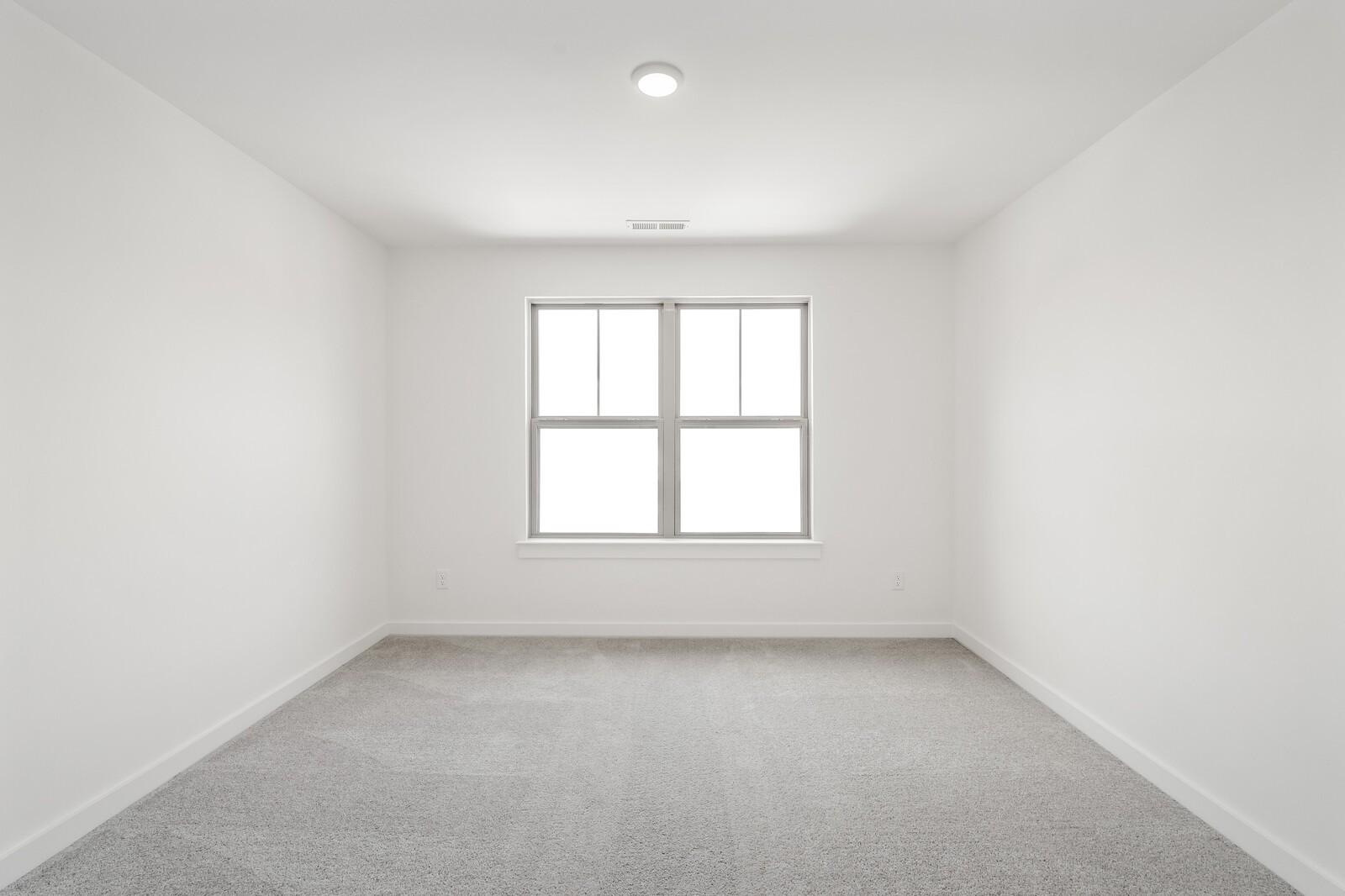 Bright, spacious bedroom with neutral carpet and natural light in The Ridgeport C floor plan at Woods Crossing, Gallatin.