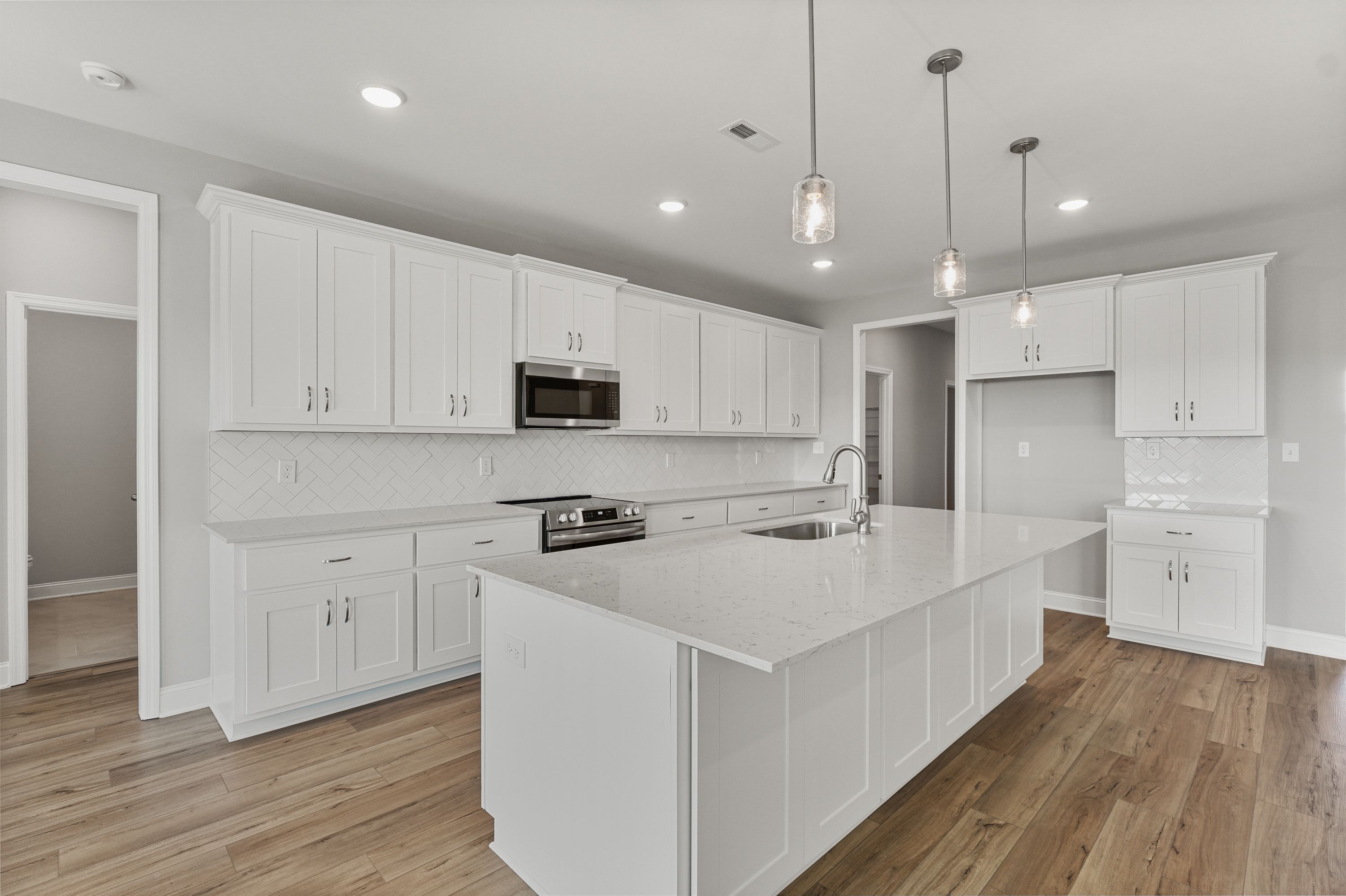 Spacious white kitchen in The Valencia with shaker cabinets, quartz island sink, stainless appliances, subway tile backsplash