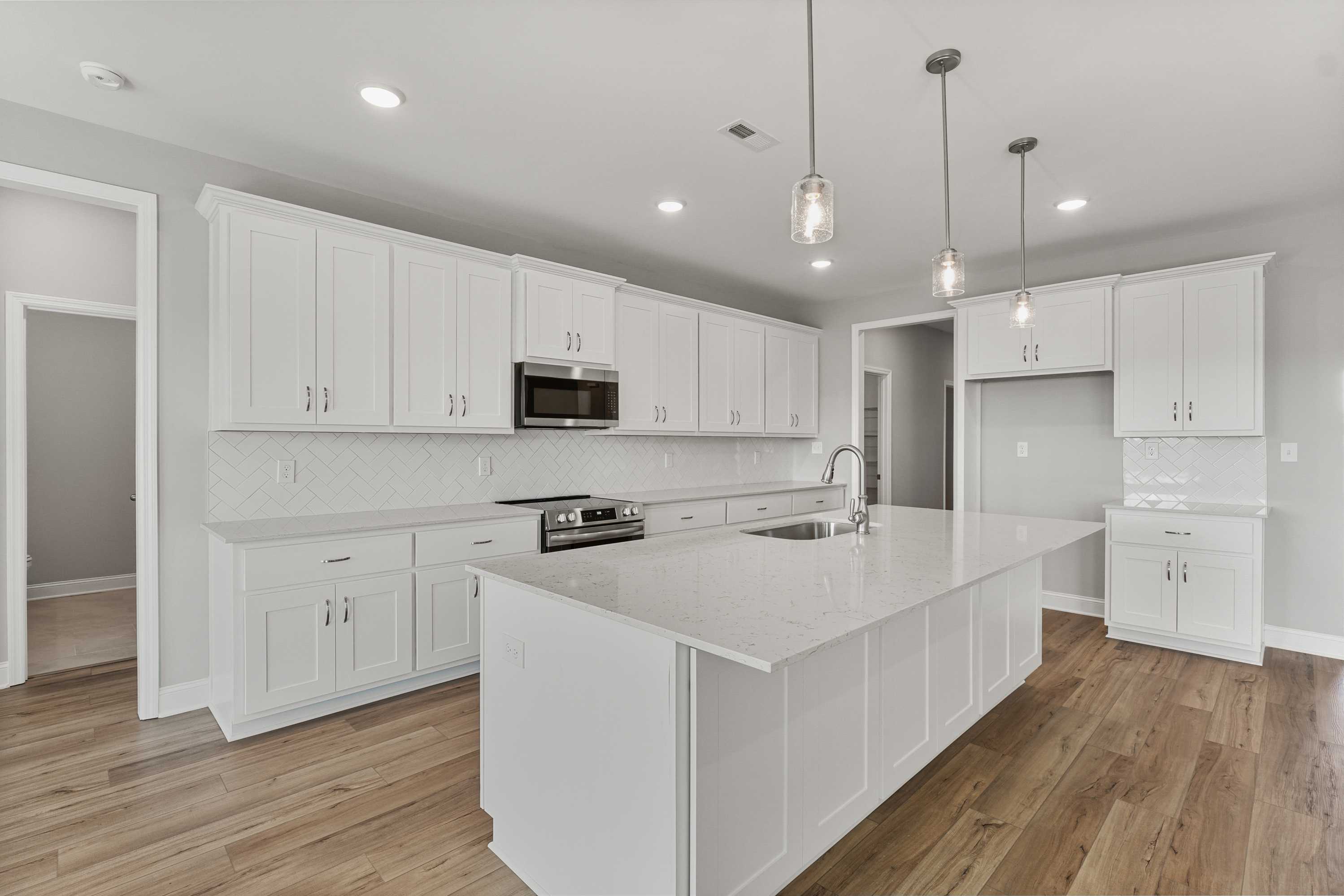 Spacious white kitchen in The Valencia with shaker cabinets, quartz island sink, stainless appliances, subway tile backsplash
