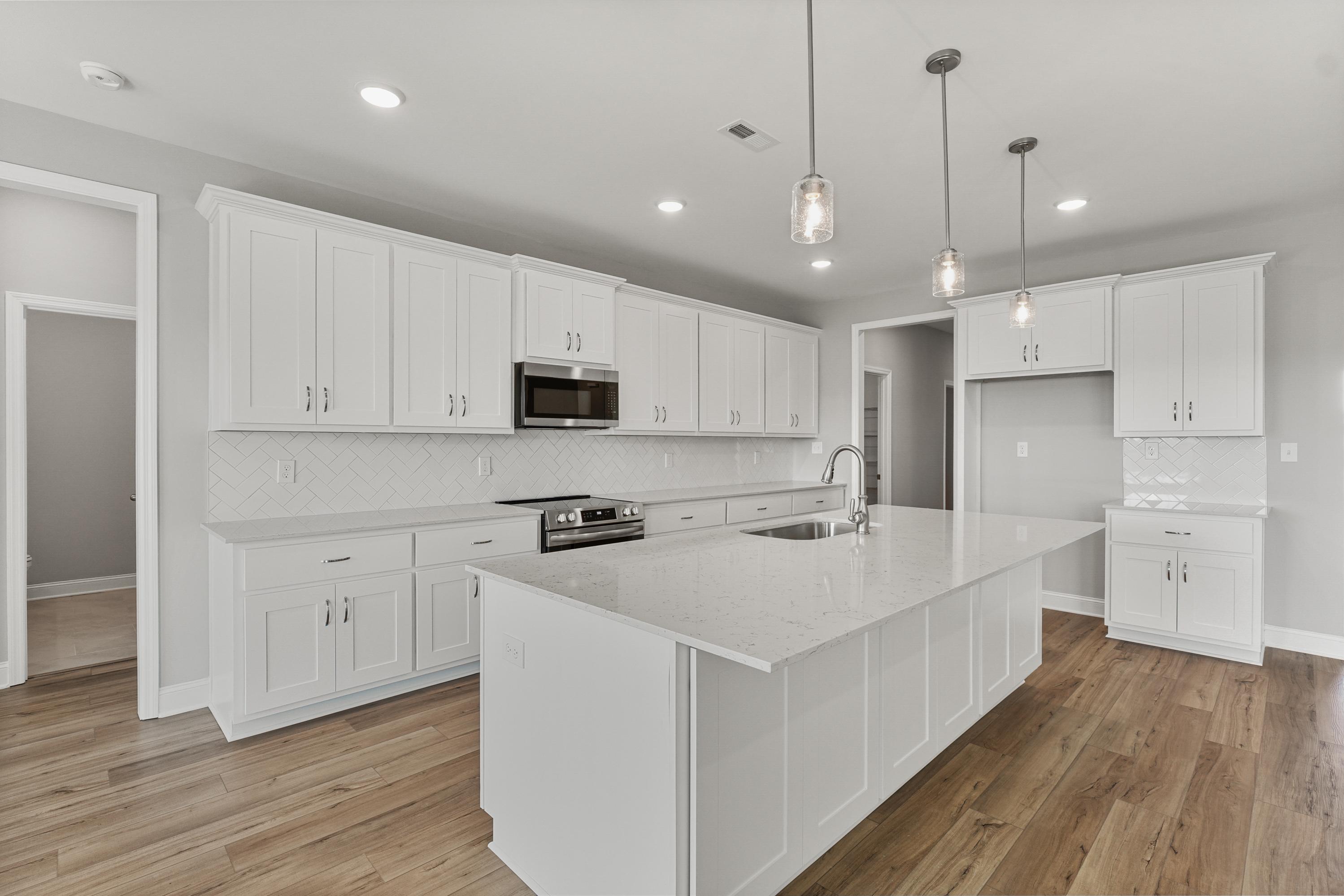 Spacious white kitchen in The Valencia with shaker cabinets, quartz island sink, stainless appliances, subway tile backsplash