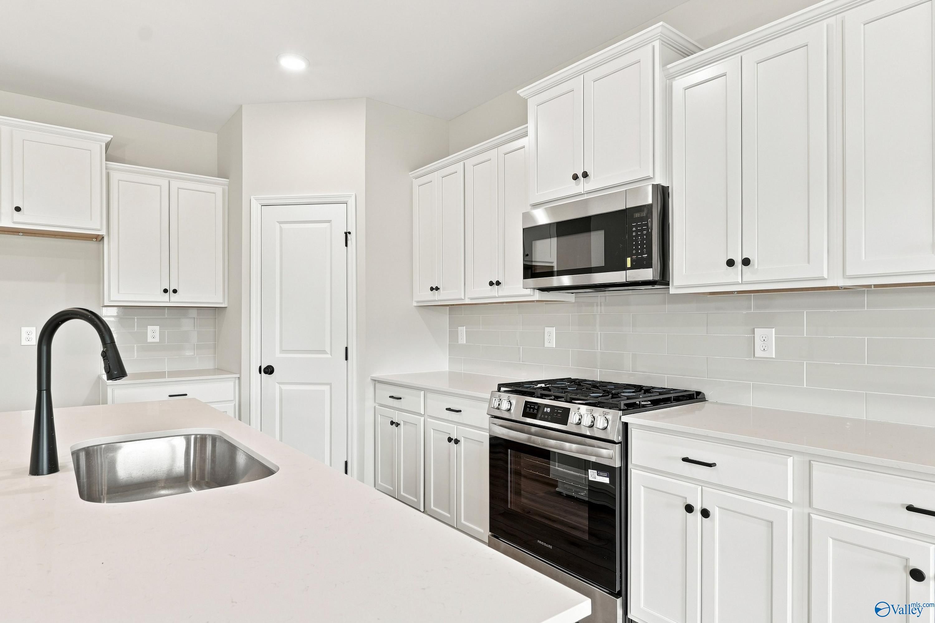 Modern kitchen with white cabinets, quartz countertops, and stainless appliances in The Rockford B floor plan, Toney, AL.