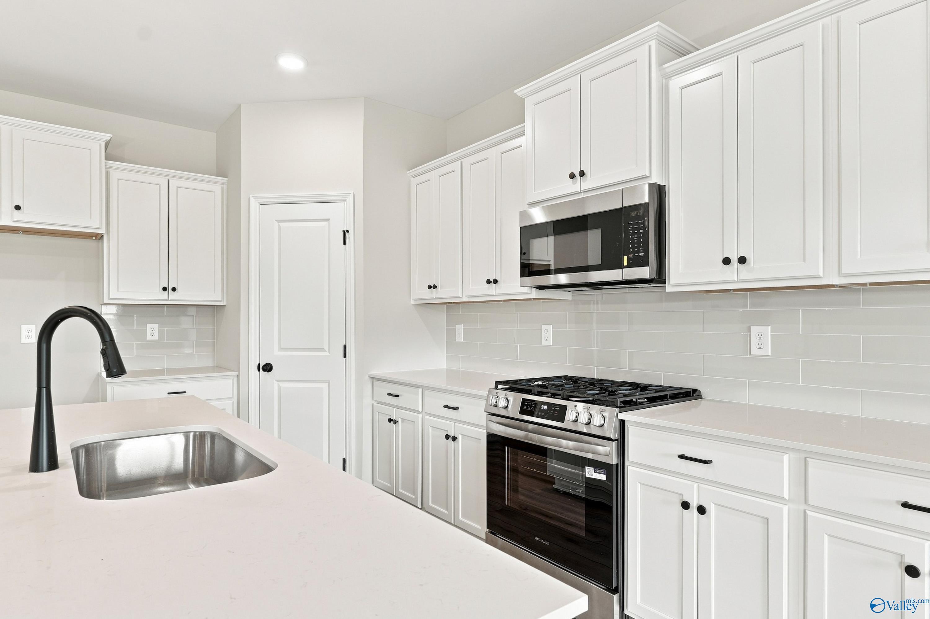 Modern kitchen with white cabinets, quartz countertops, and stainless appliances in The Rockford B floor plan, Toney, AL.