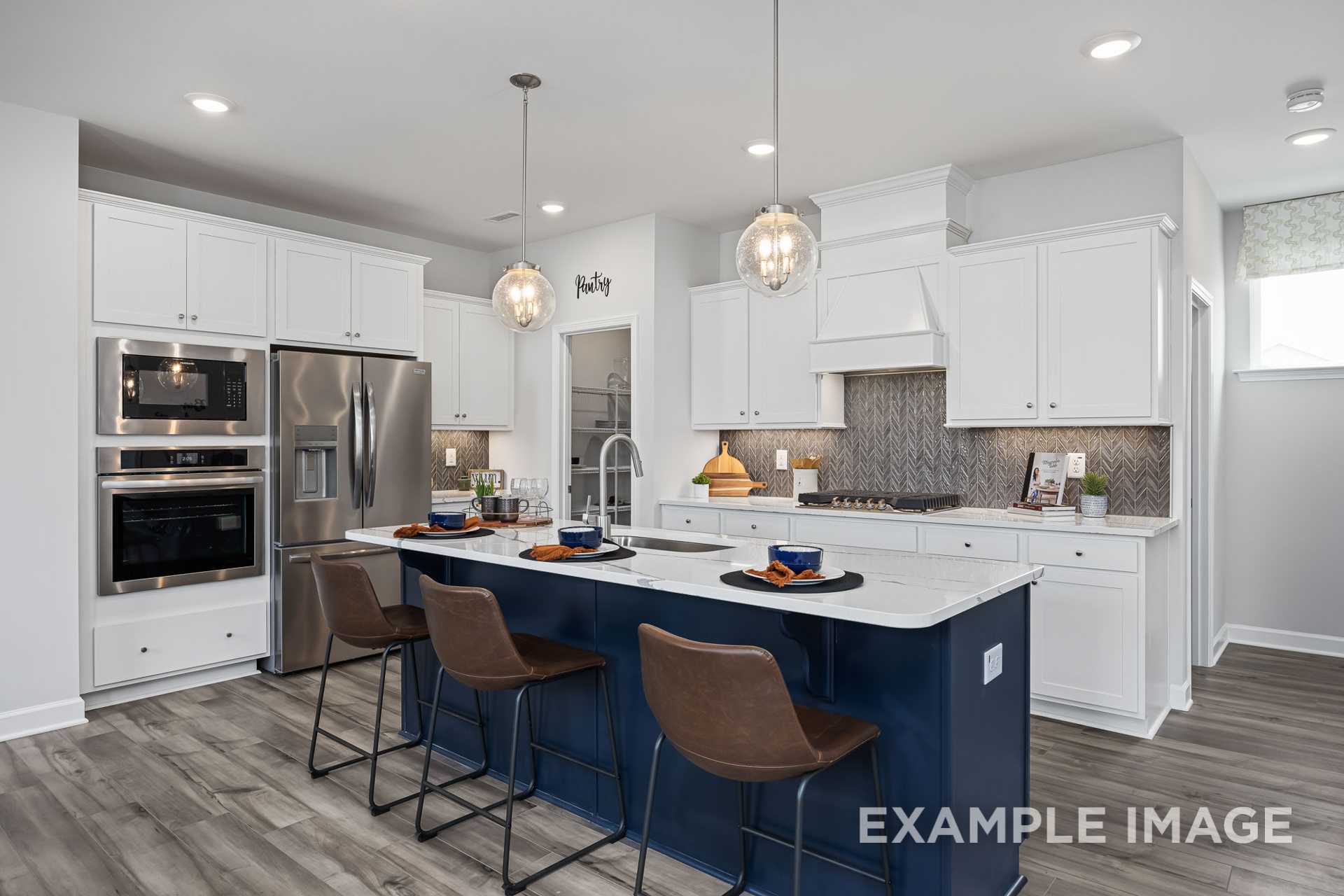 Spacious kitchen in The Adalynn A featuring white cabinets, stainless steel appliances, navy island with bar stools