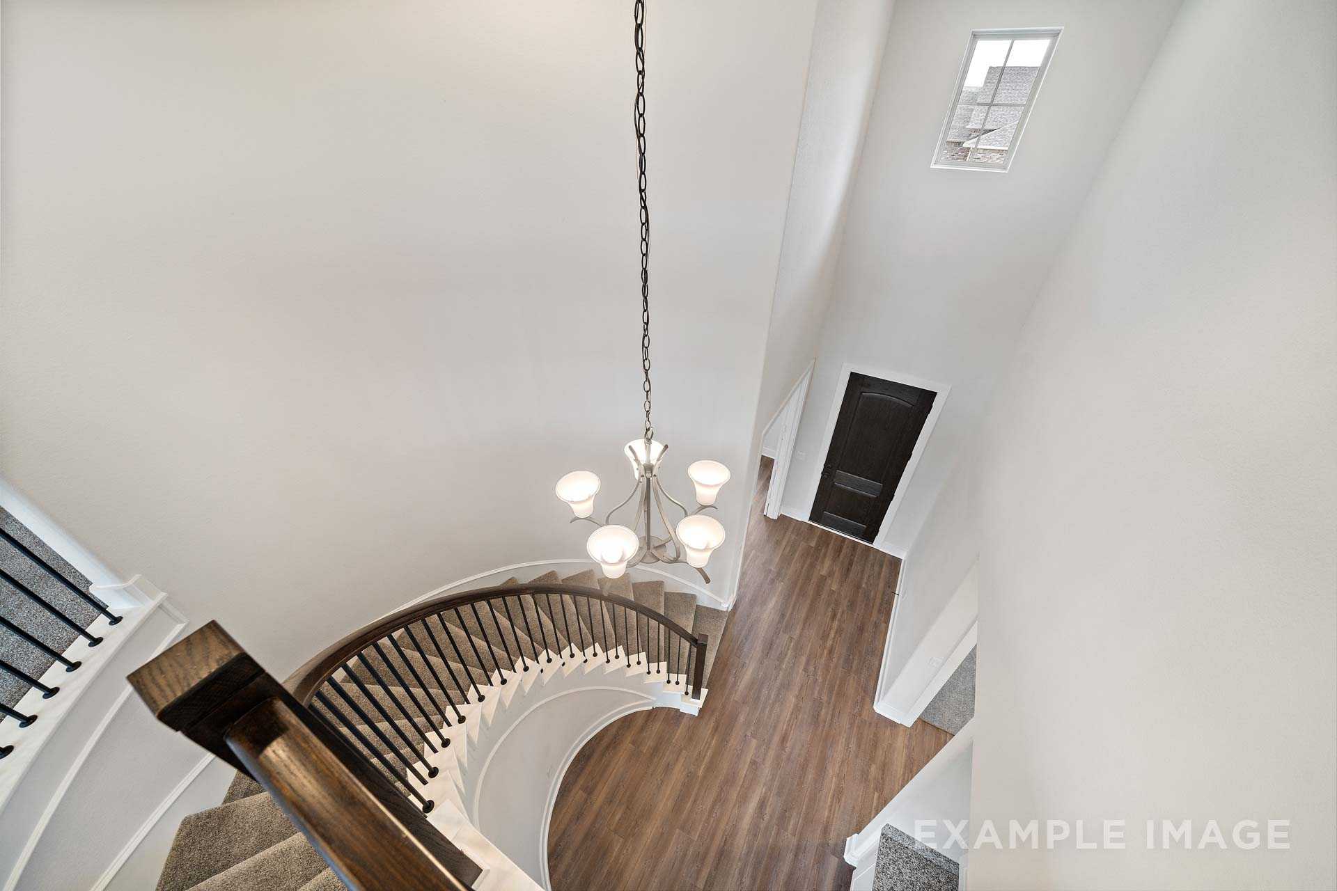 Spiral staircase with black wrought iron railing and crystal chandelier in The Victoria A two-story foyer by Davidson Homes