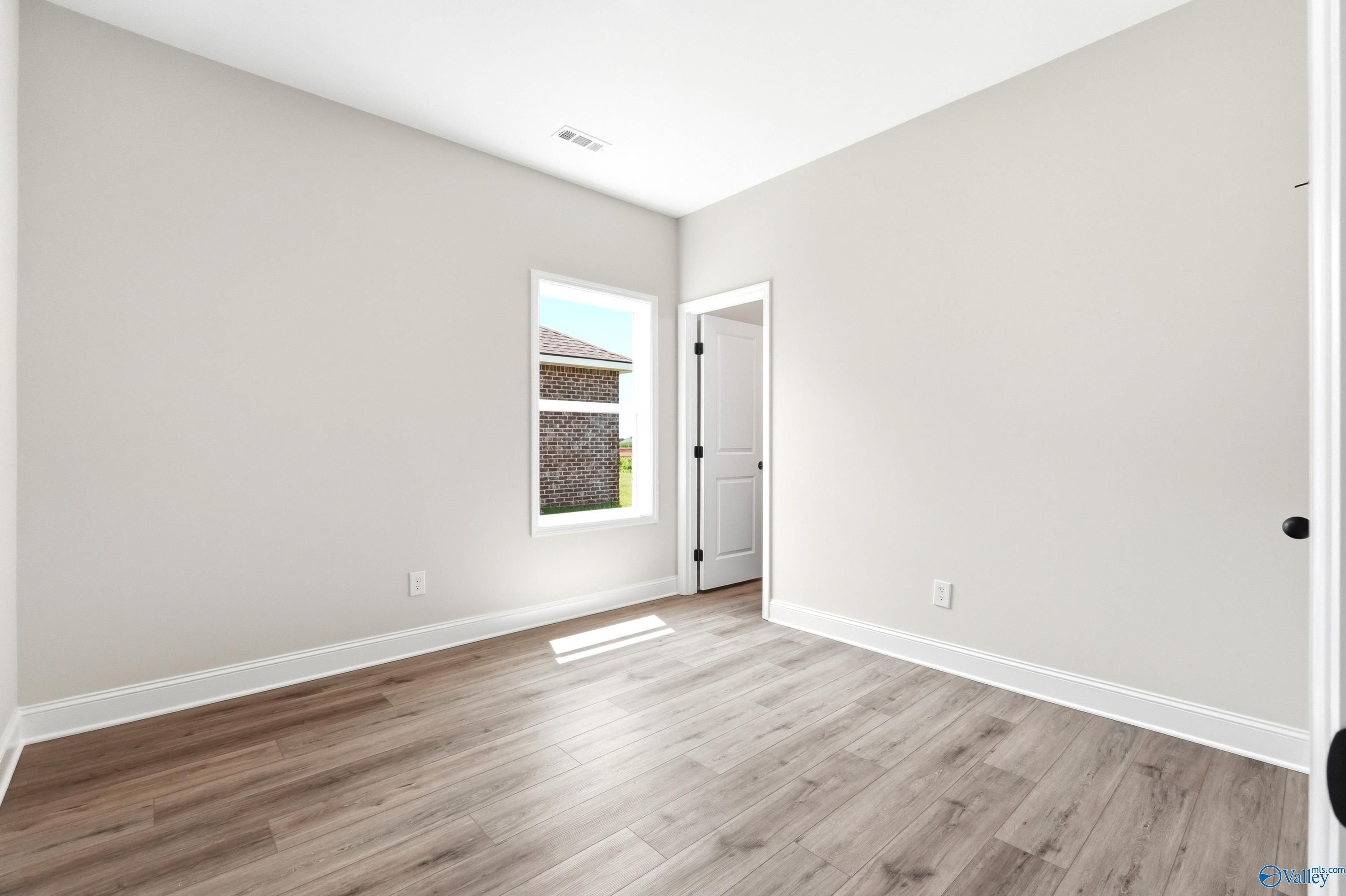 Bright, neutral-toned bedroom with wood-look flooring in The Daphne floor plan by Davidson Homes in Hazel Green, Alabama.
