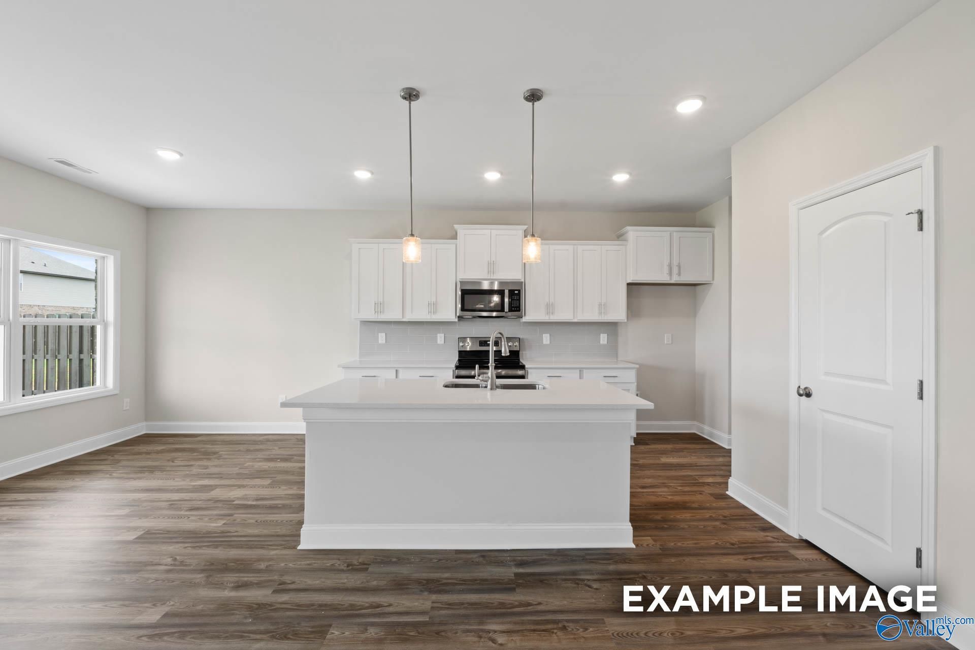 Modern kitchen with white cabinets, island, and wood-style flooring in The Shelby B plan at Jaguar Hills, Huntsville.