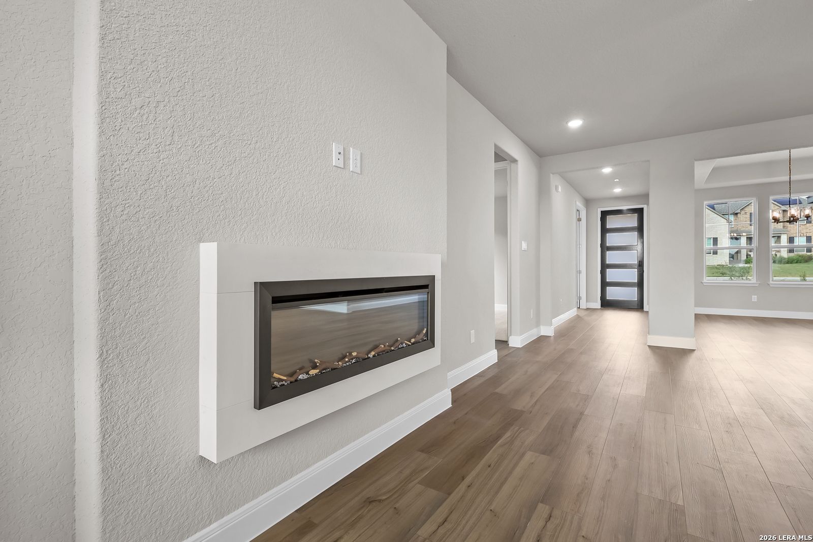 Modern linear fireplace with wood-look tile flooring in open living area of Davidson Homes The Foster E, Castroville, Texas