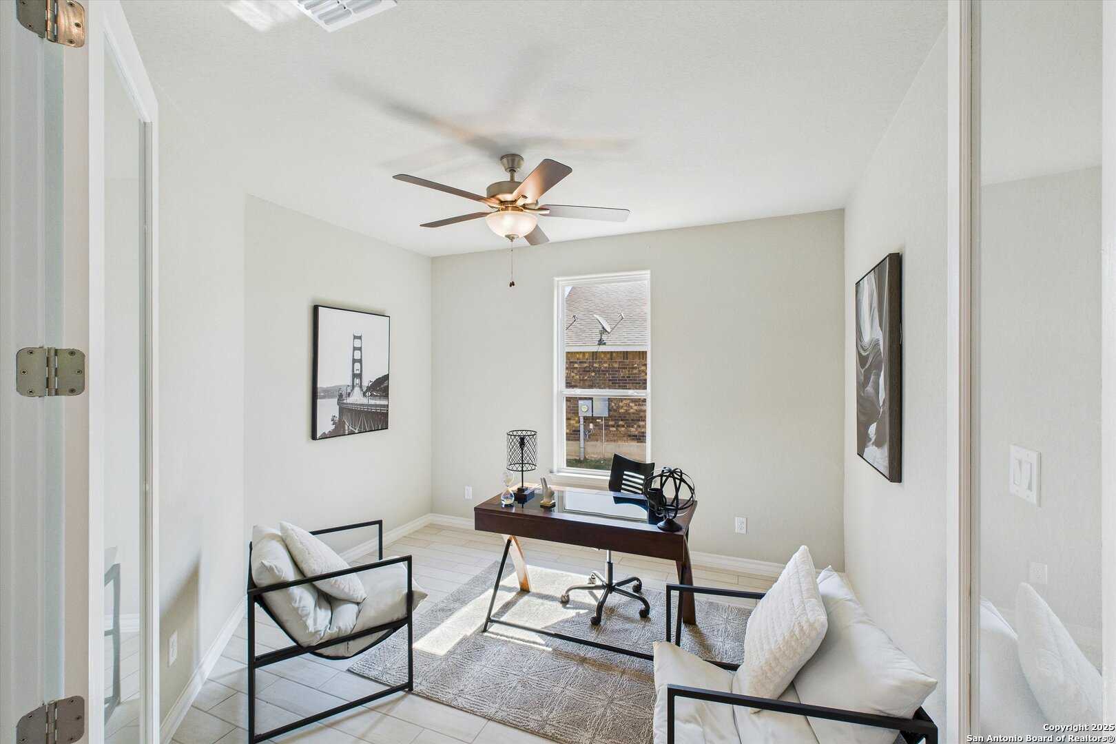 Modern home office with wooden desk, armchairs, ceiling fan, and artwork in Davidson Homes The Jennings H, Ladera, San Antonio