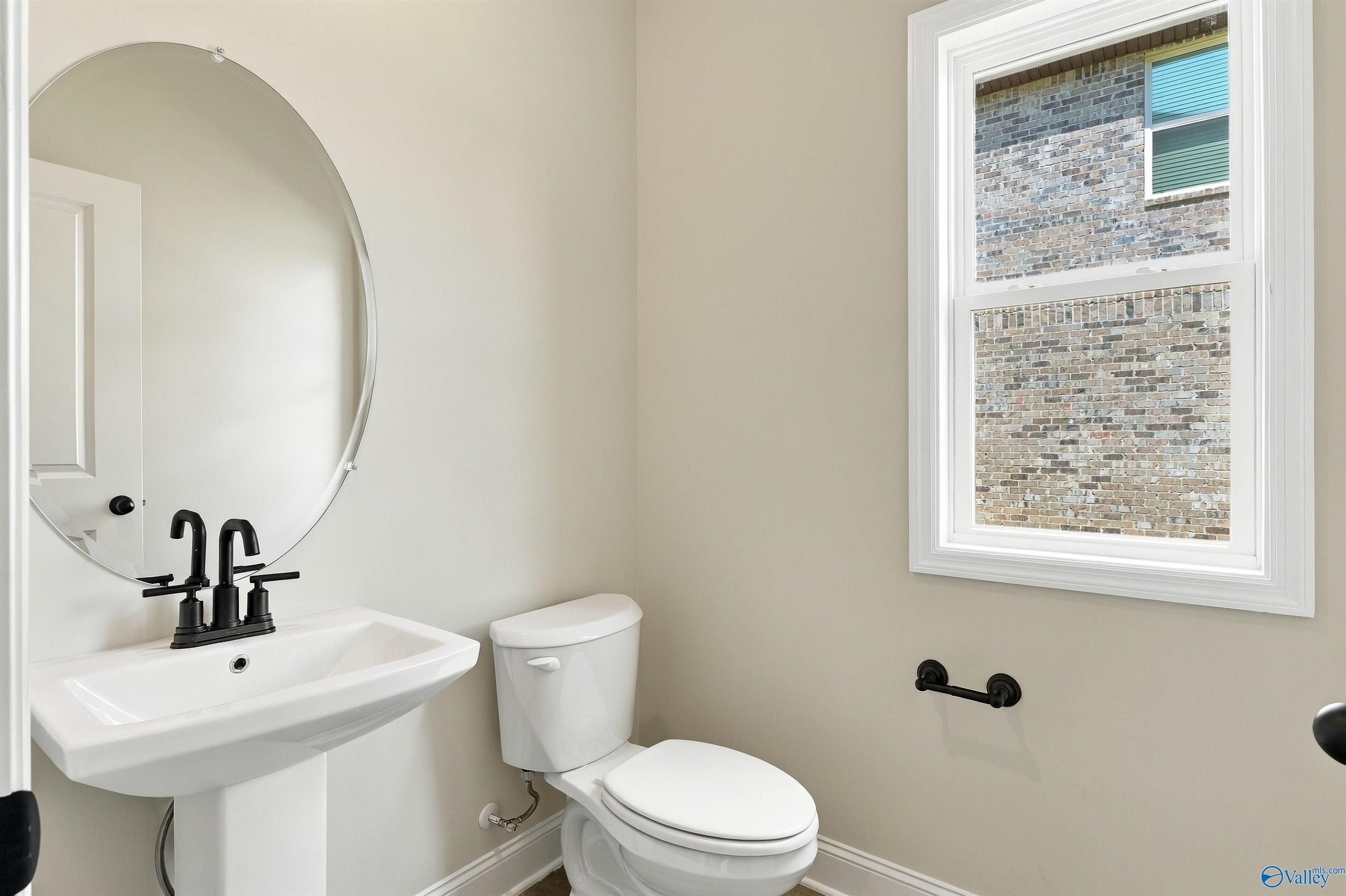 Half bath with pedestal sink, matte black fixtures, and round mirror in Davidson Homes The Shelby A, The Meadows, Athens, Alabama