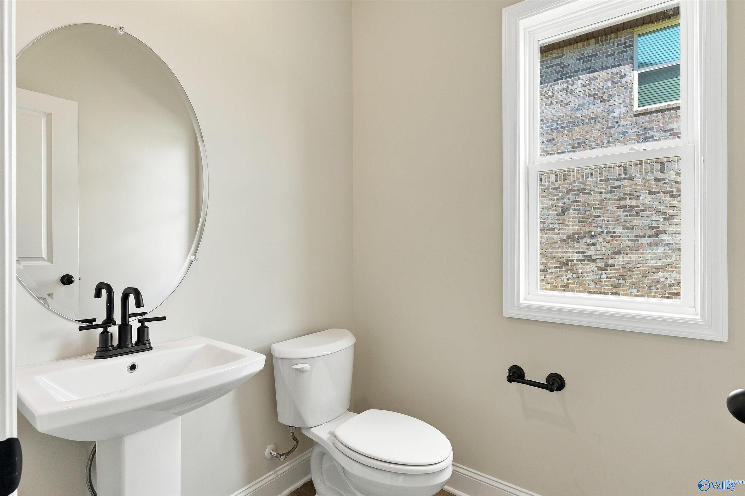 Half bath with pedestal sink, matte black fixtures, and round mirror in Davidson Homes The Shelby A, The Meadows, Athens, Alabama