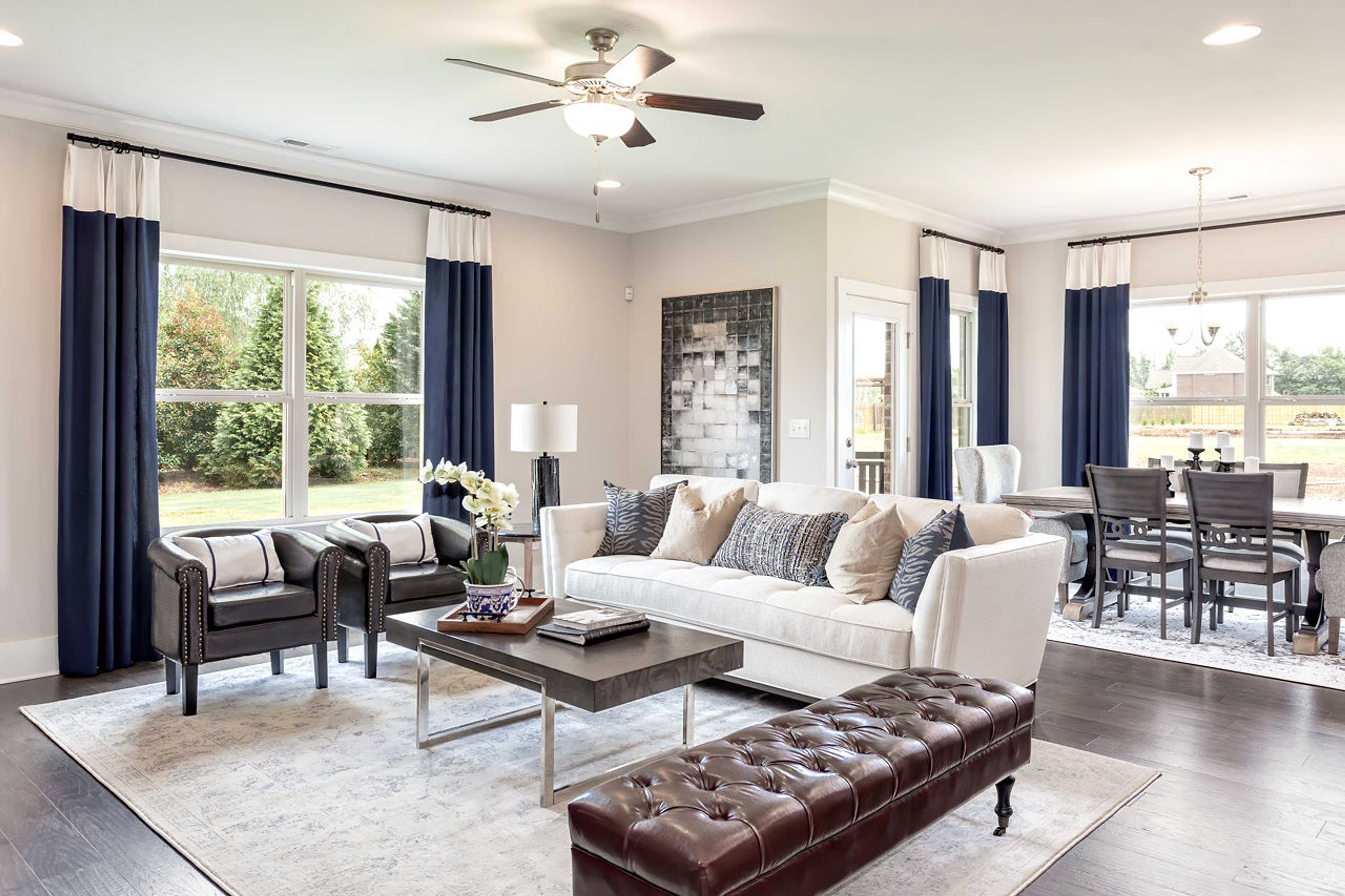 Open-concept living room at Williams Pointe in Huntsville Alabama with white sofa, leather chairs, hardwood floors and navy curtains