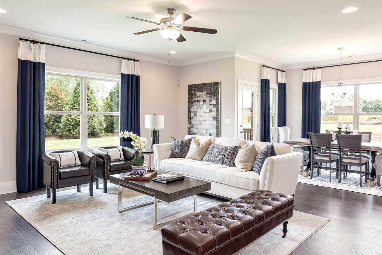 Open-concept living room at Williams Pointe in Huntsville Alabama with white sofa, leather chairs, hardwood floors and navy curtains