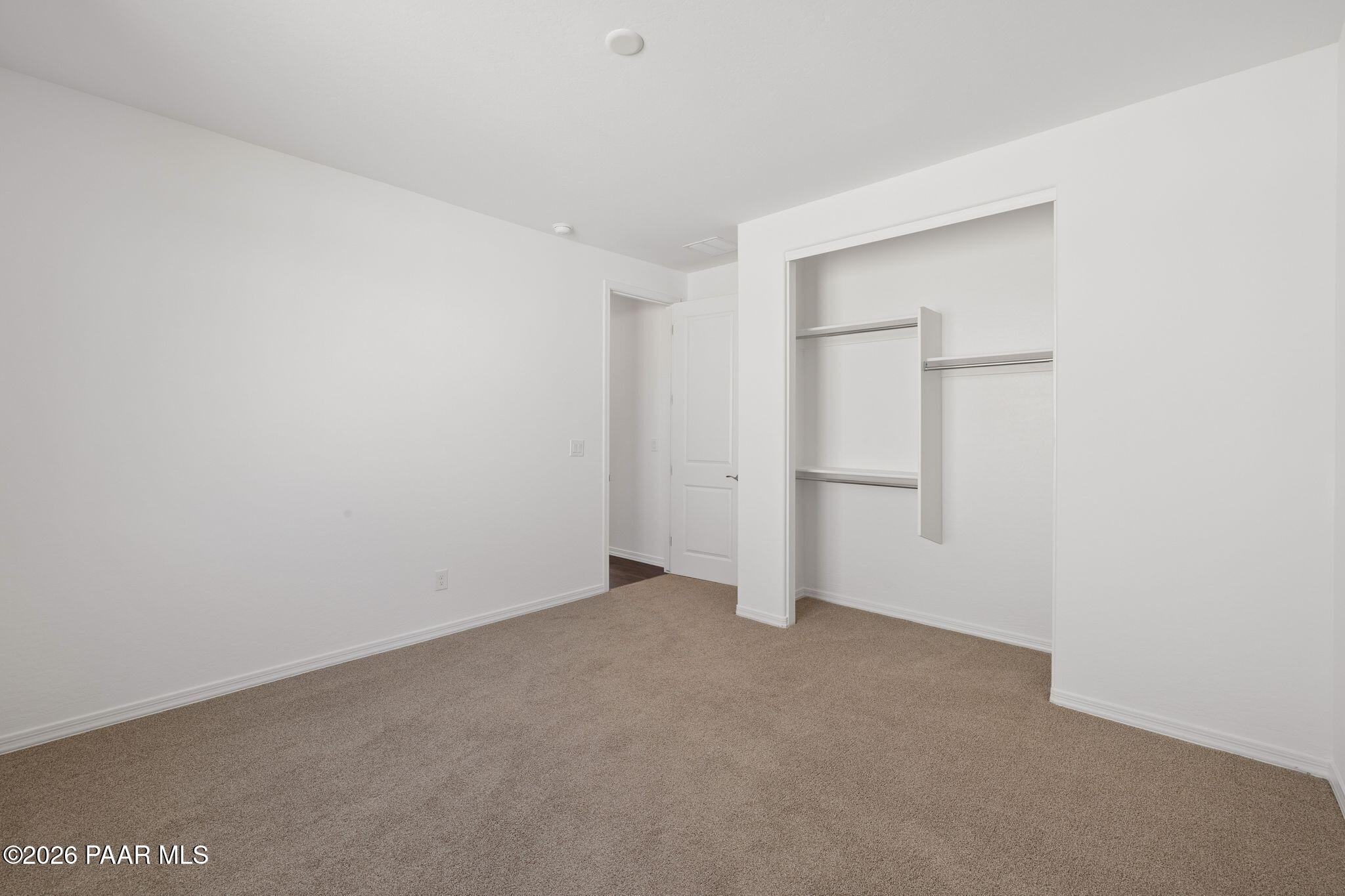 Spacious empty bedroom with beige carpet, white walls, and built-in shelving in Davidson Homes The Monarch A, Prescott AZ