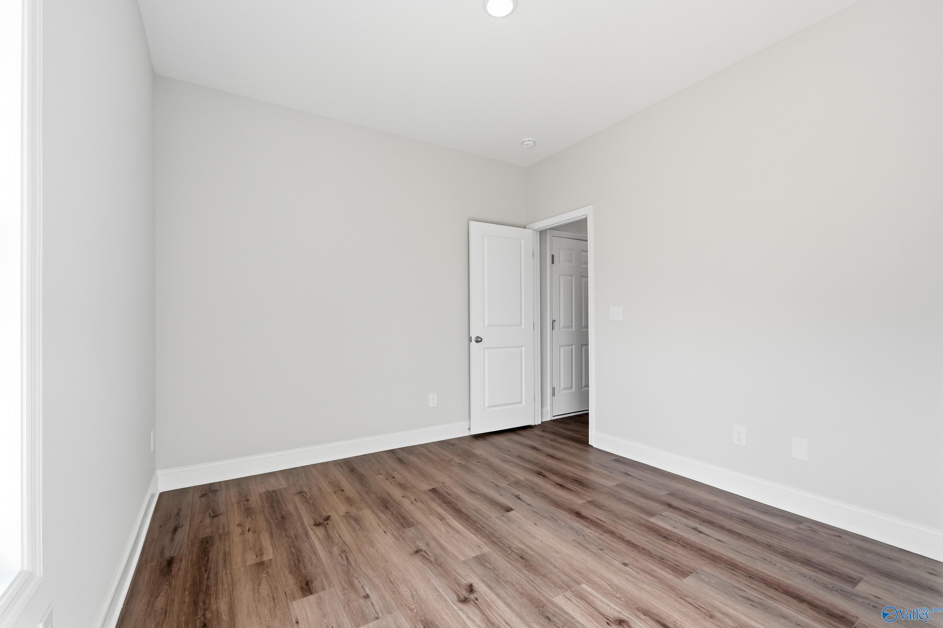 Bright bedroom with light gray walls, open white door, and hardwood floors in Davidson Homes The Daphne C, Toney, Alabama