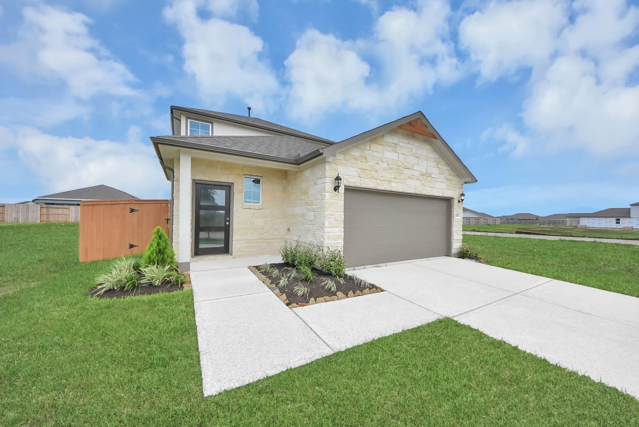 Stone and stucco exterior with 2-car garage and landscaped yard of The San Marcos E new home in Emberly, Beasley, Texas