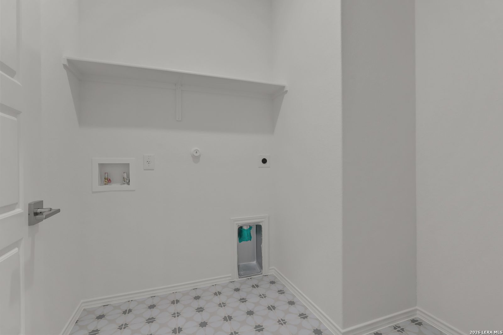 Spacious laundry room with built-in shelf, washer-dryer hookups, teal pet door, and star-pattern tile floor in The Glenwood E home, Elmendorf Texas