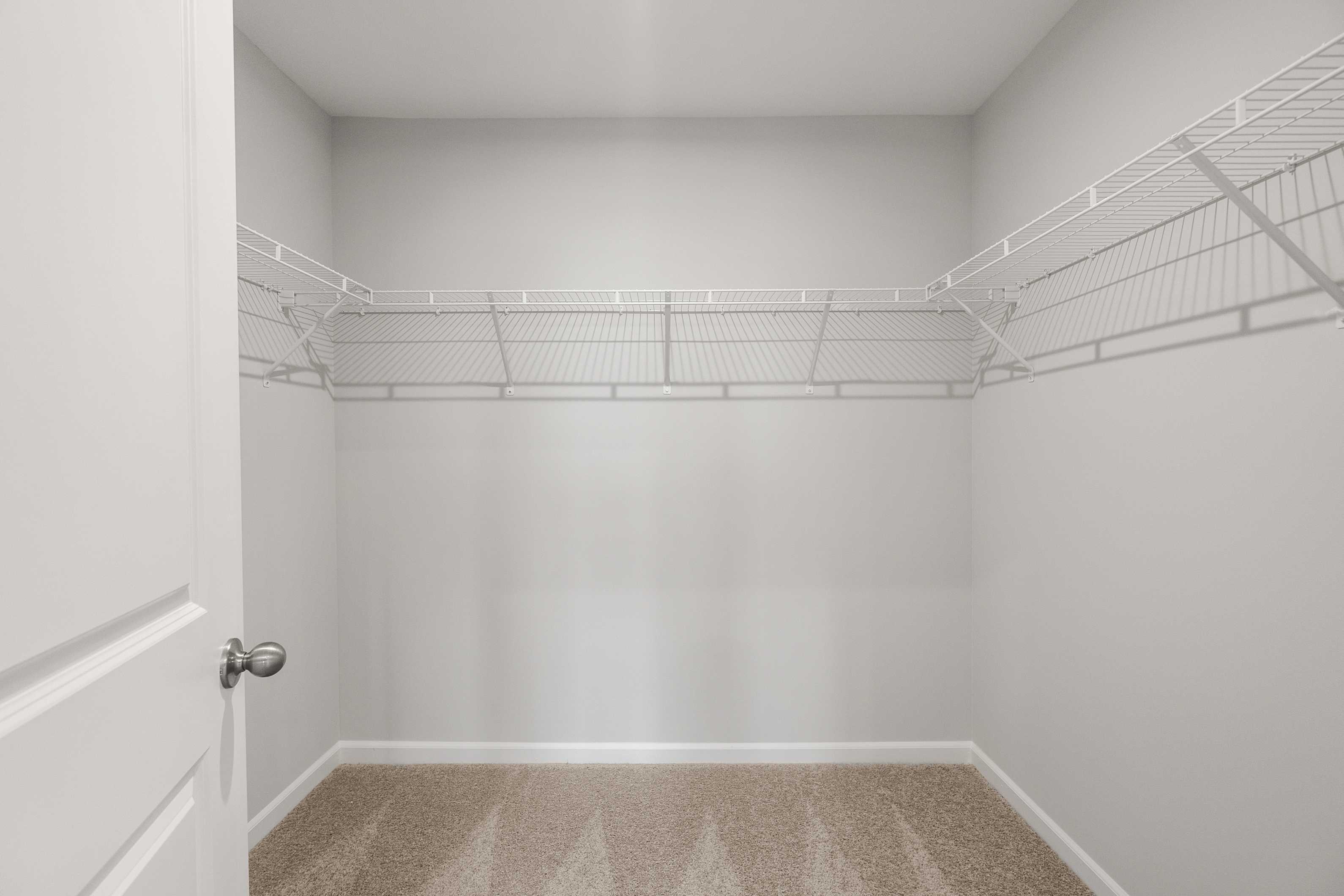 Spacious walk-in closet in The Durant A master suite with white wire shelving, carpeted floor, and open door