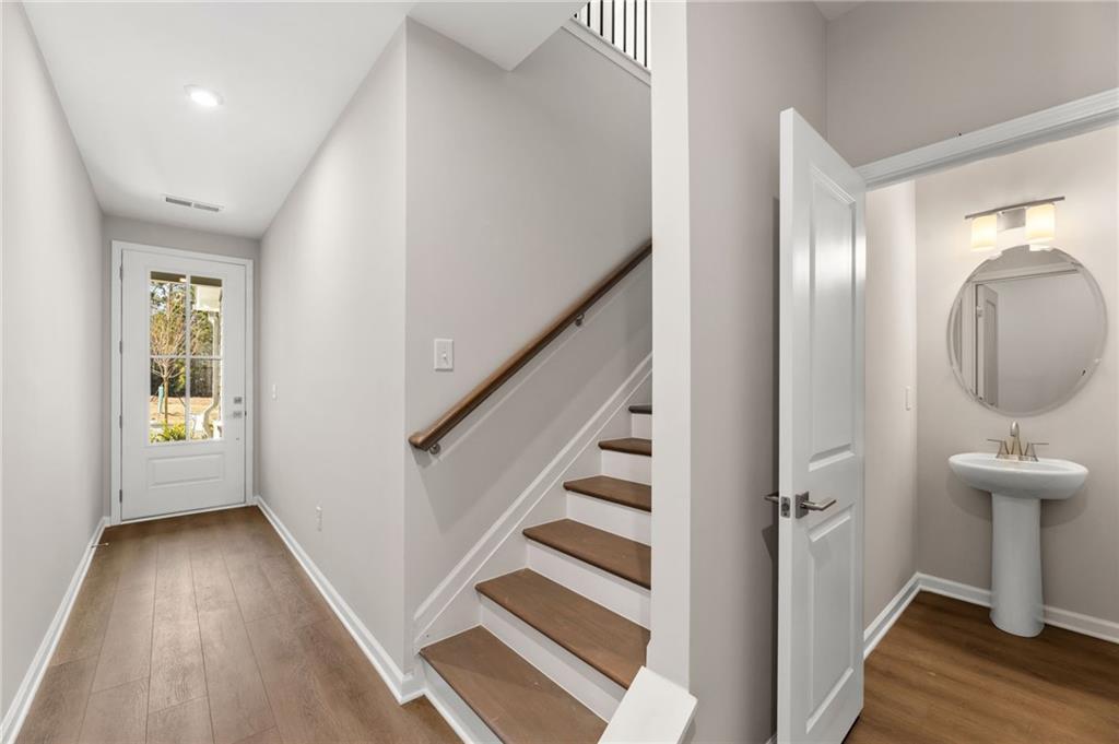 Bright entry hallway with hardwood floors, white front door, staircase, and adjacent powder room with pedestal sink in Davidson Homes The Marion A, Winder, Georgia