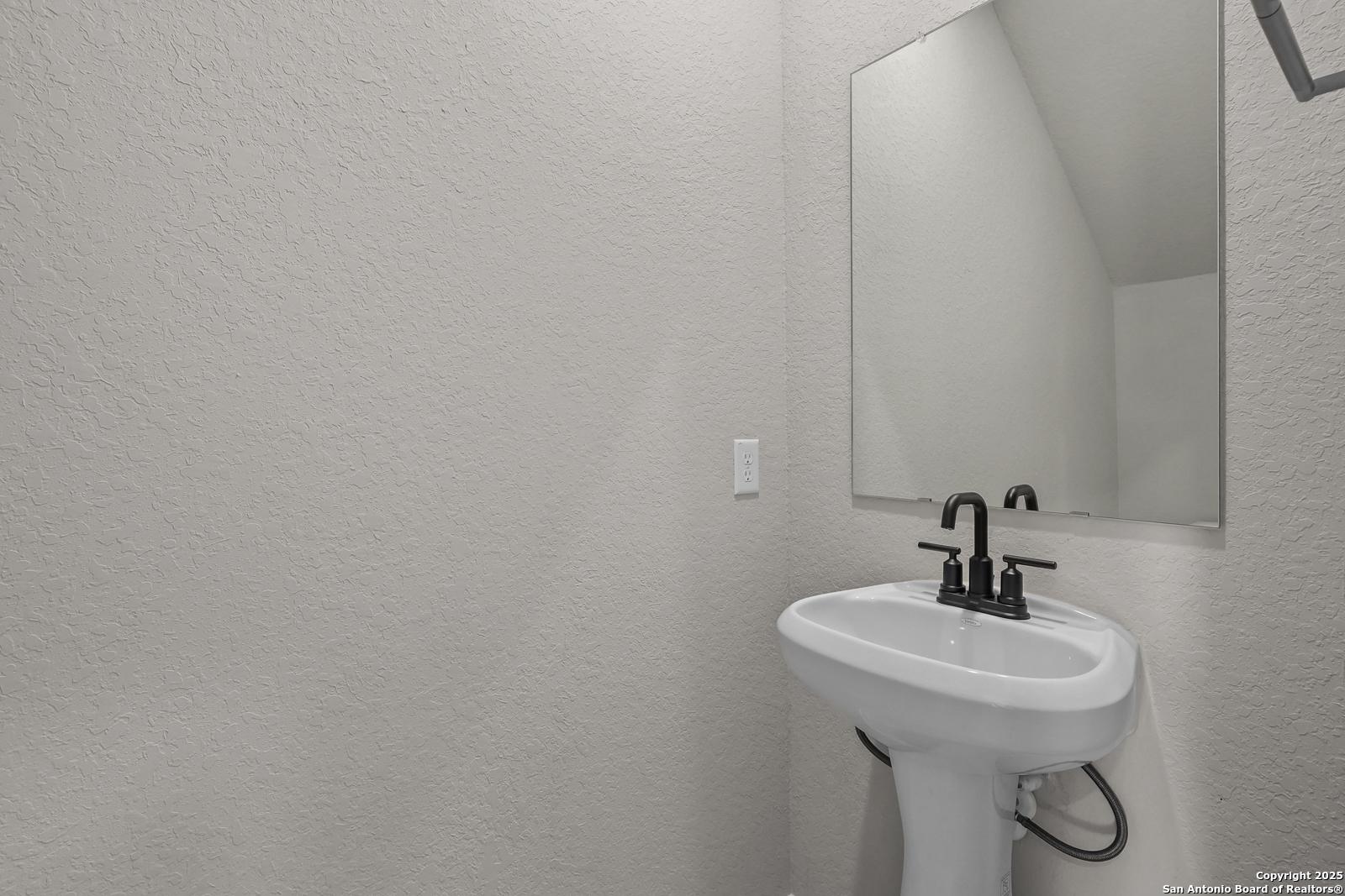 Elegant powder room with white pedestal sink, black faucet, and frameless mirror in Davidson Homes The Brazos C, San Antonio