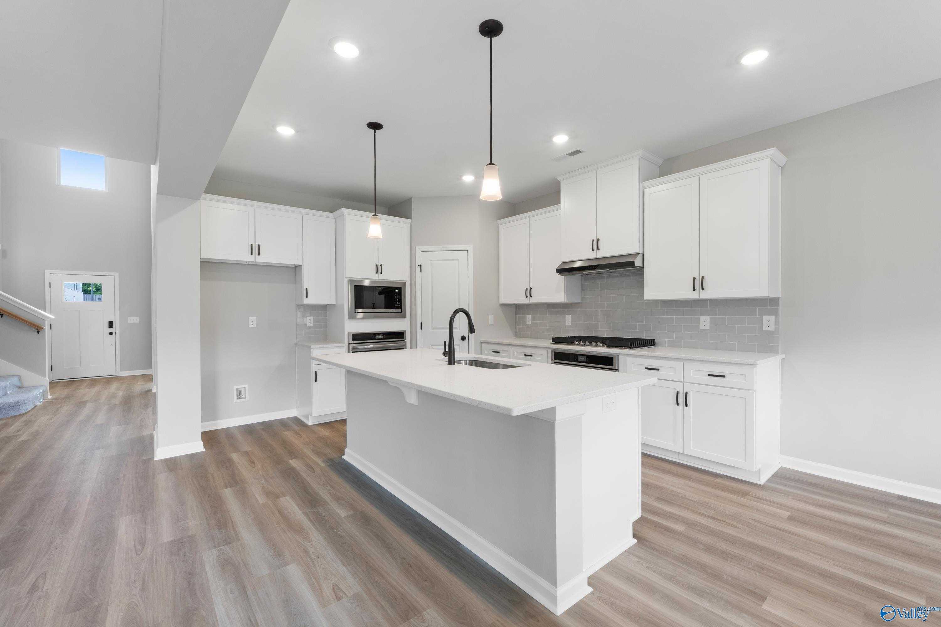 Bright open-concept kitchen with white cabinets, quartz island, stainless appliances, and hardwood floors in Davidson Homes The Dorado, Huntsville, AL