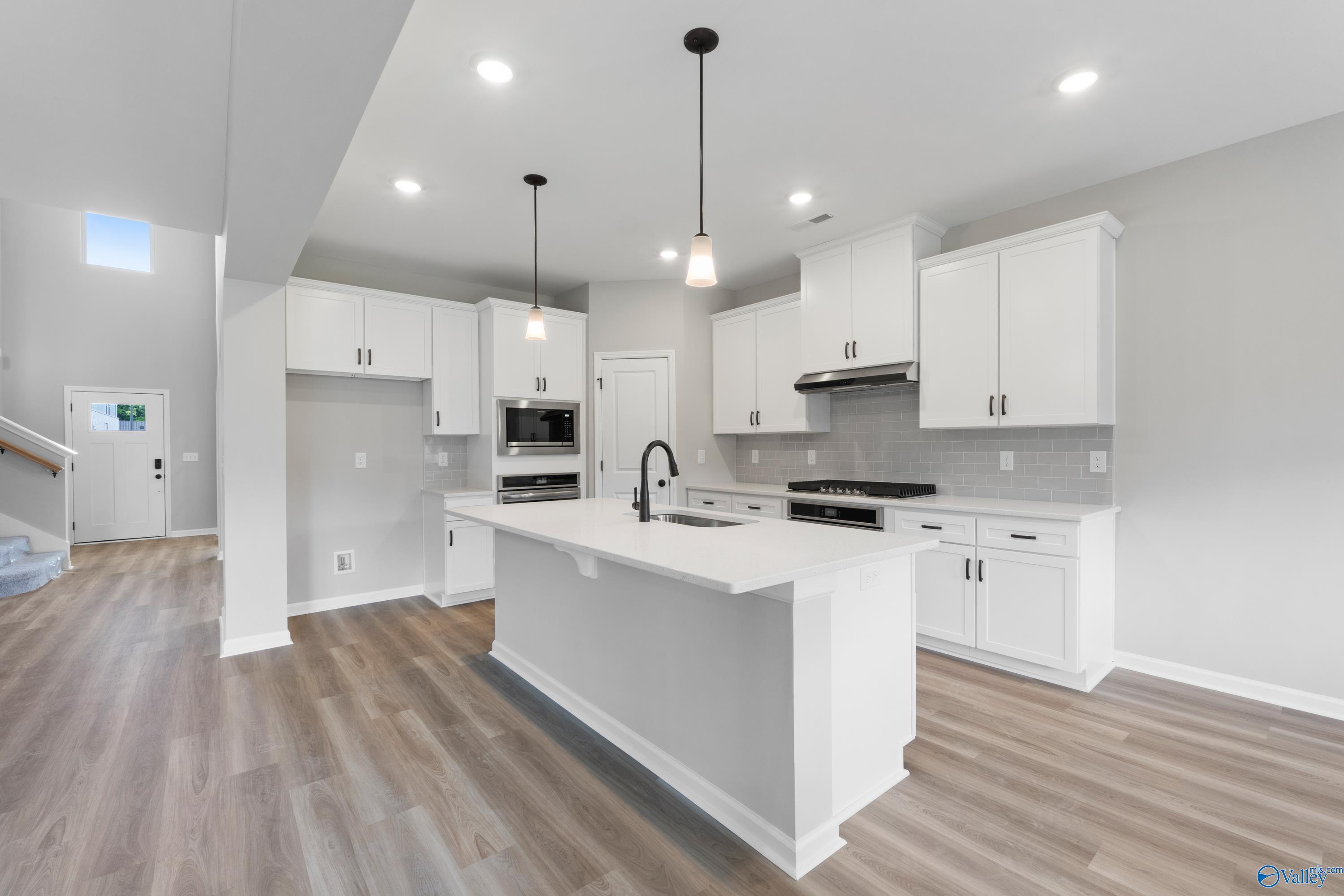Bright open-concept kitchen with white cabinets, quartz island, stainless appliances, and hardwood floors in Davidson Homes The Dorado, Huntsville, AL