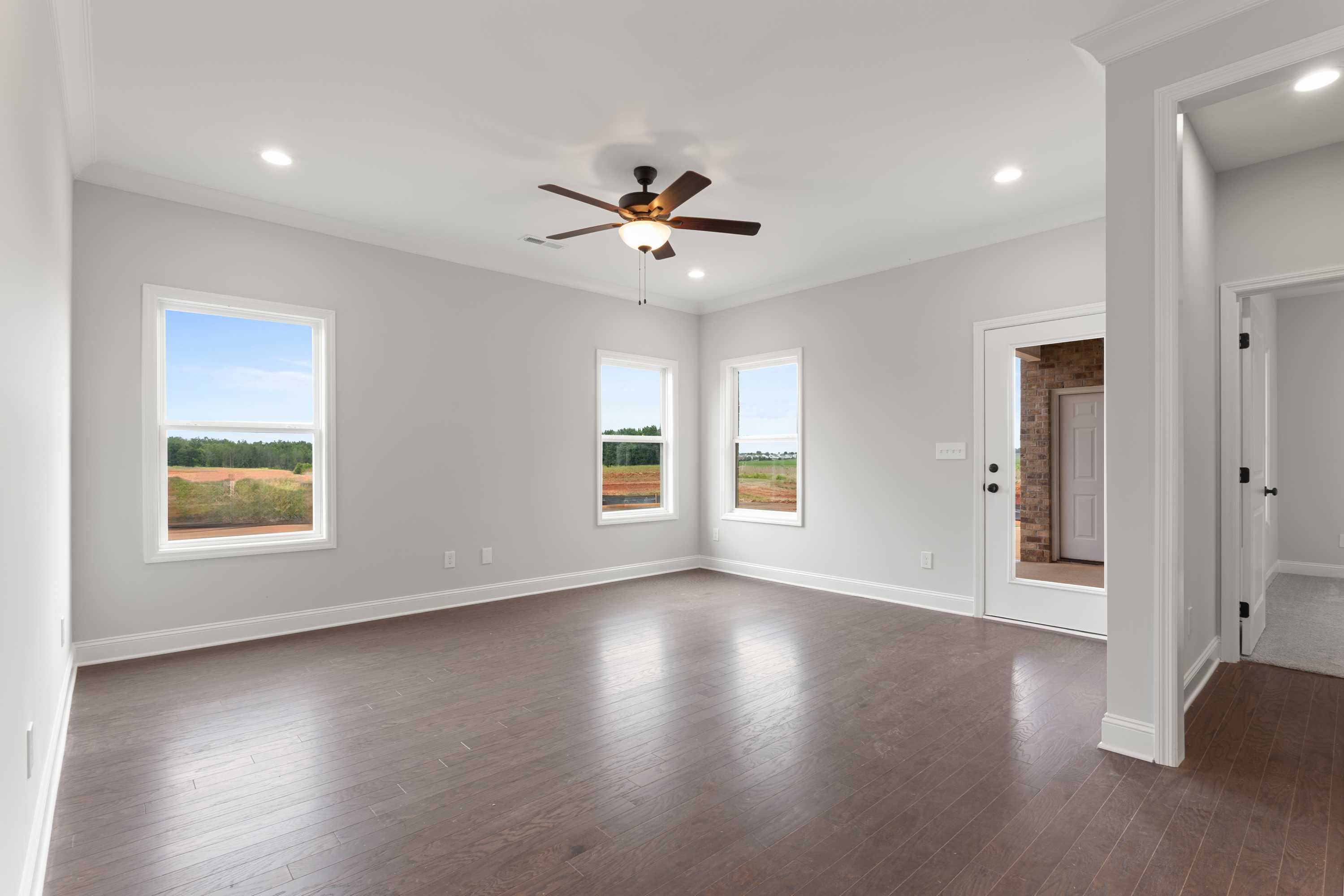 Spacious master bedroom in The Copeland with large windows overlooking green fields, ceiling fan, hardwood floors, and neutral walls