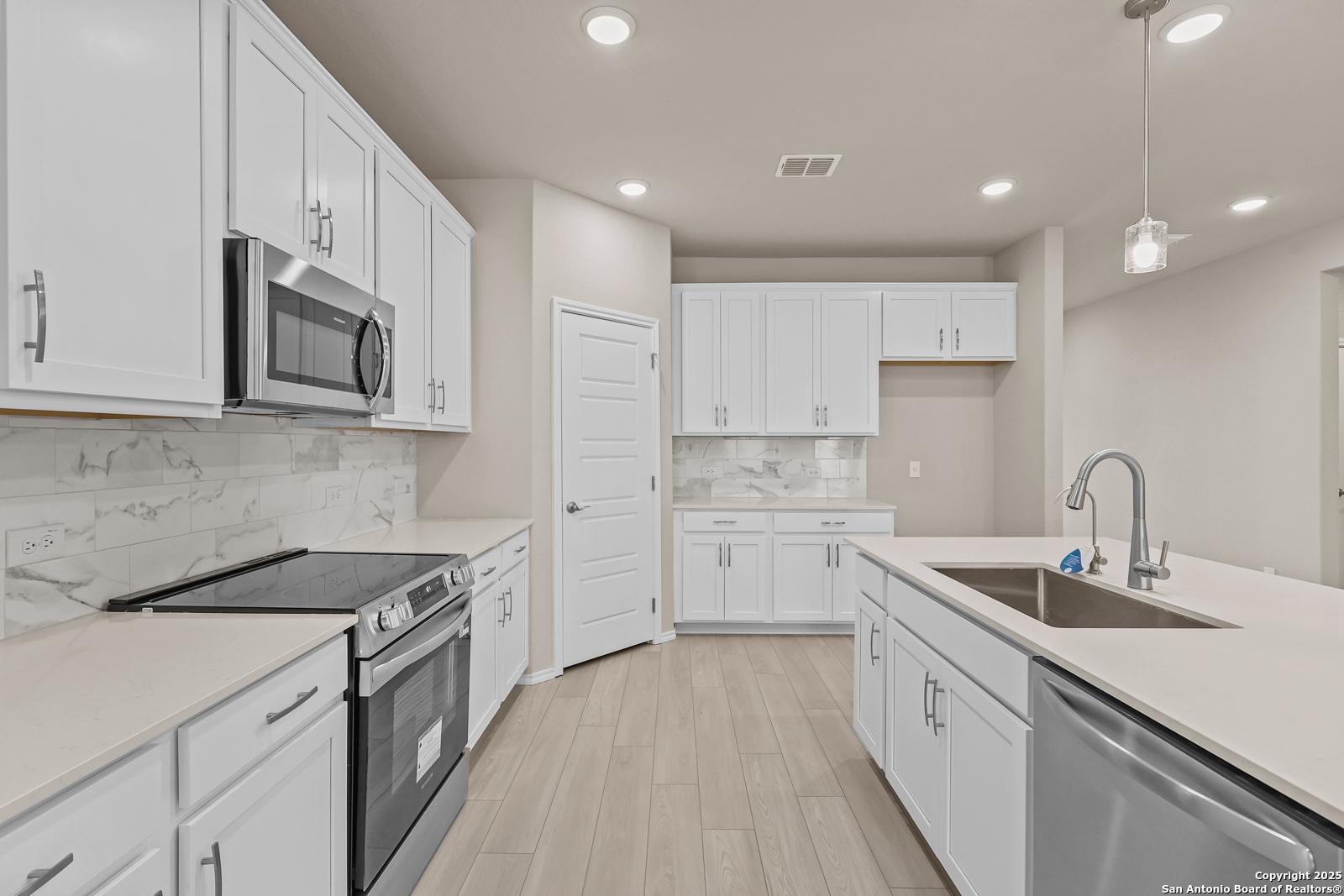 Modern white kitchen with quartz counters, marble backsplash, stainless appliances, and island sink in Davidson Homes The Douglas G, San Antonio